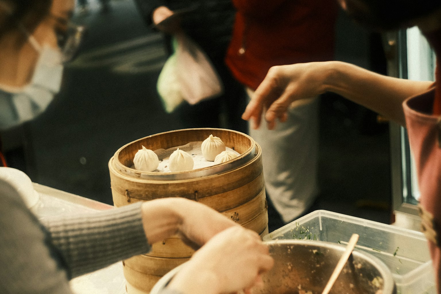 Manos alcanzando dumplings de una vaporera de bambú