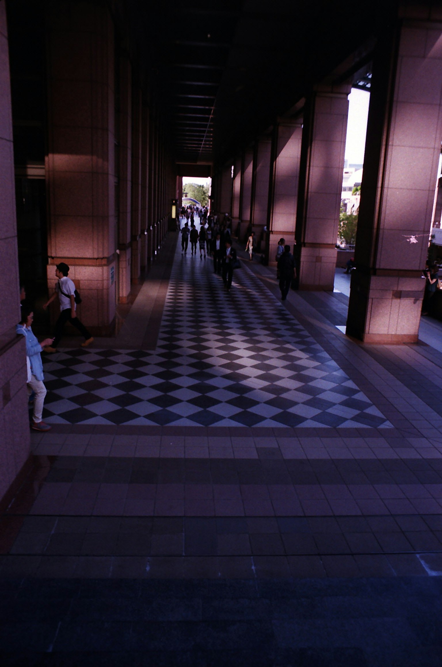 Des gens marchant sous une large arcade avec des ombres sur le sol décoré