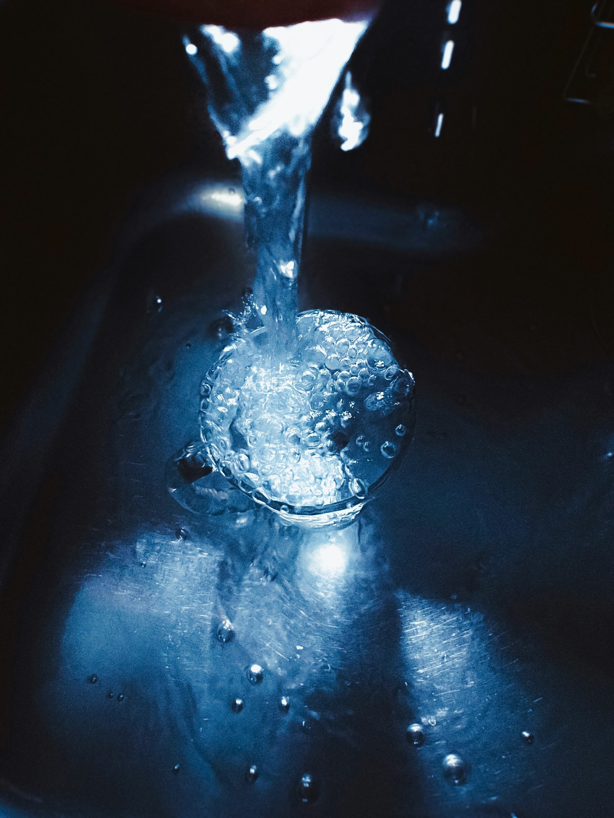 青い光の下で水があふれるガラスのコップ