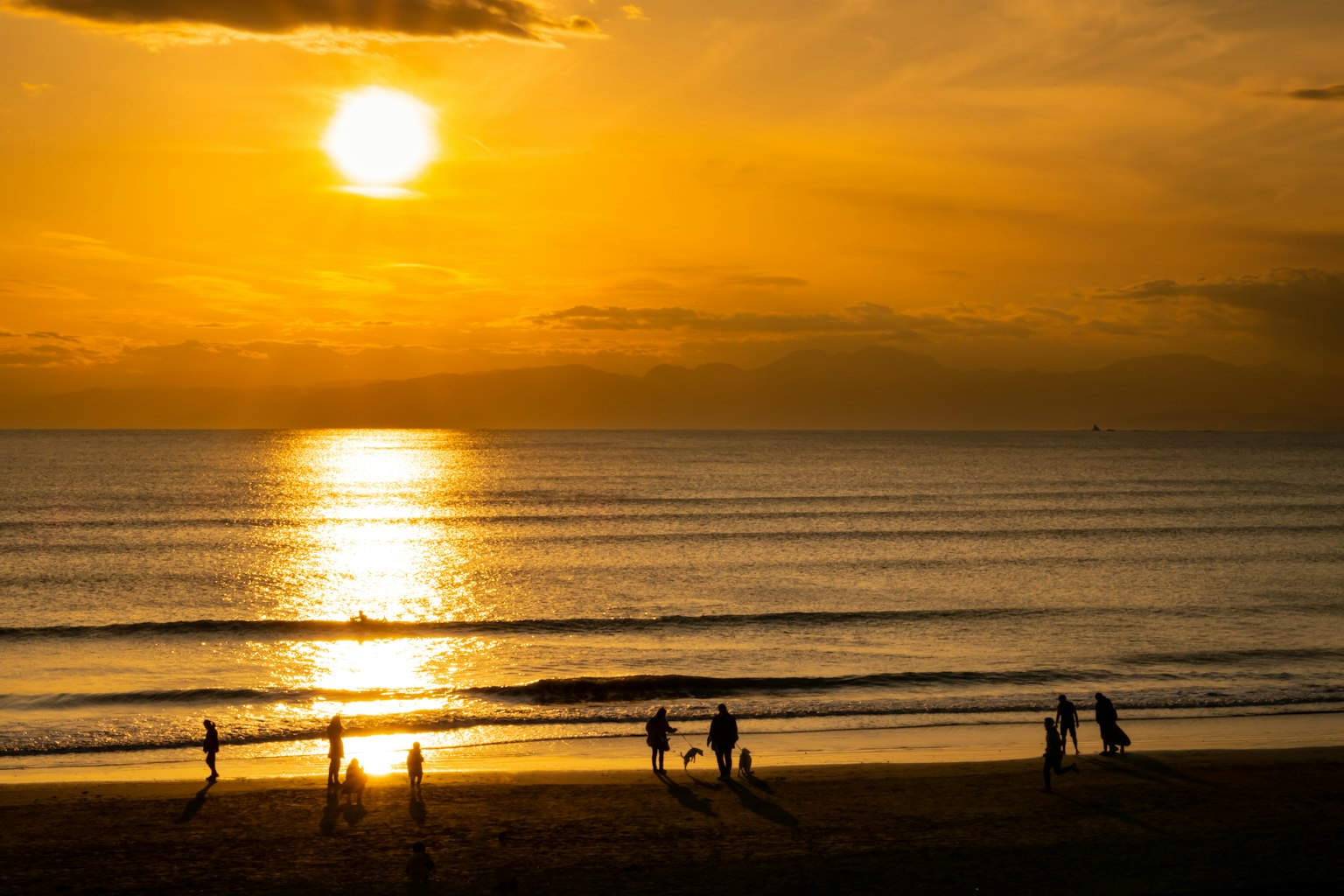 Menschen, die bei Sonnenuntergang an einem Strand mit goldenen Reflexionen im Wasser spazieren