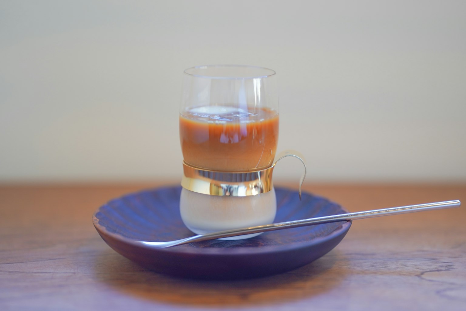 Layered coffee drink in a transparent glass with cream on a wooden plate