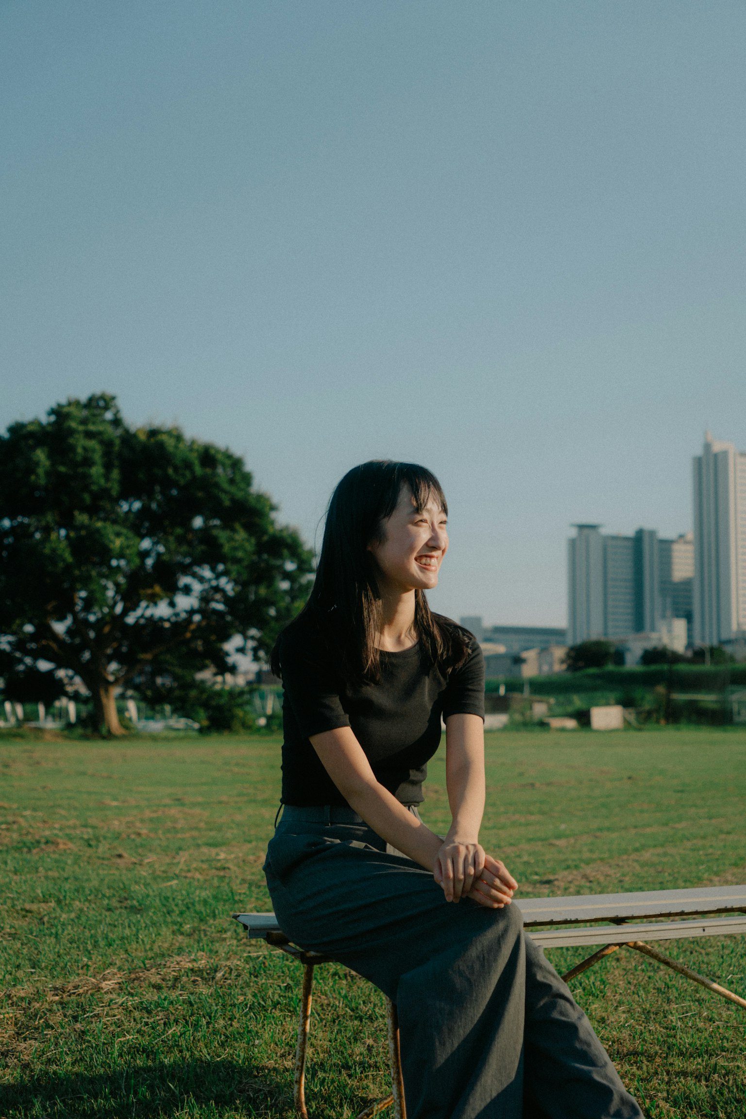 一名女性坐在公園裡，背景是城市天際線和一棵大樹