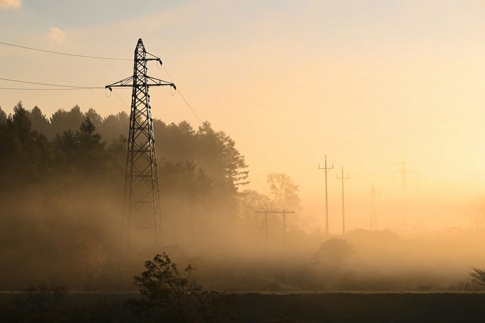 torres de transmisión eléctrica y cables en un atardecer brumoso
