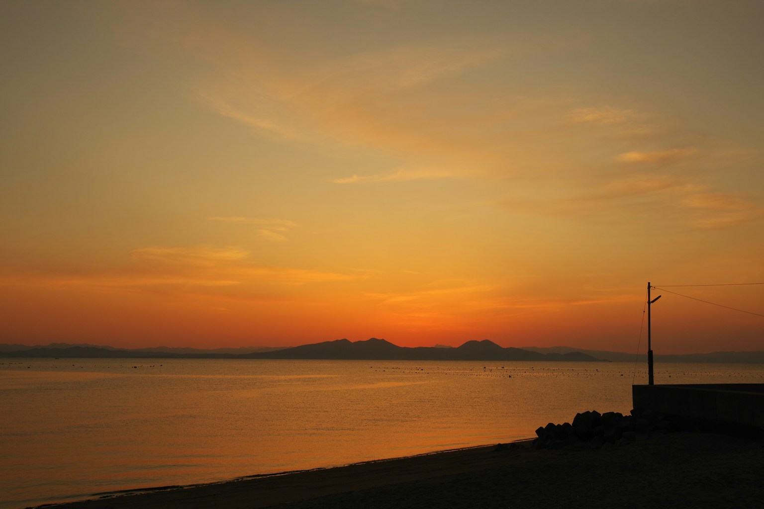Scenic view of a sunset over the calm sea with silhouettes of distant hills