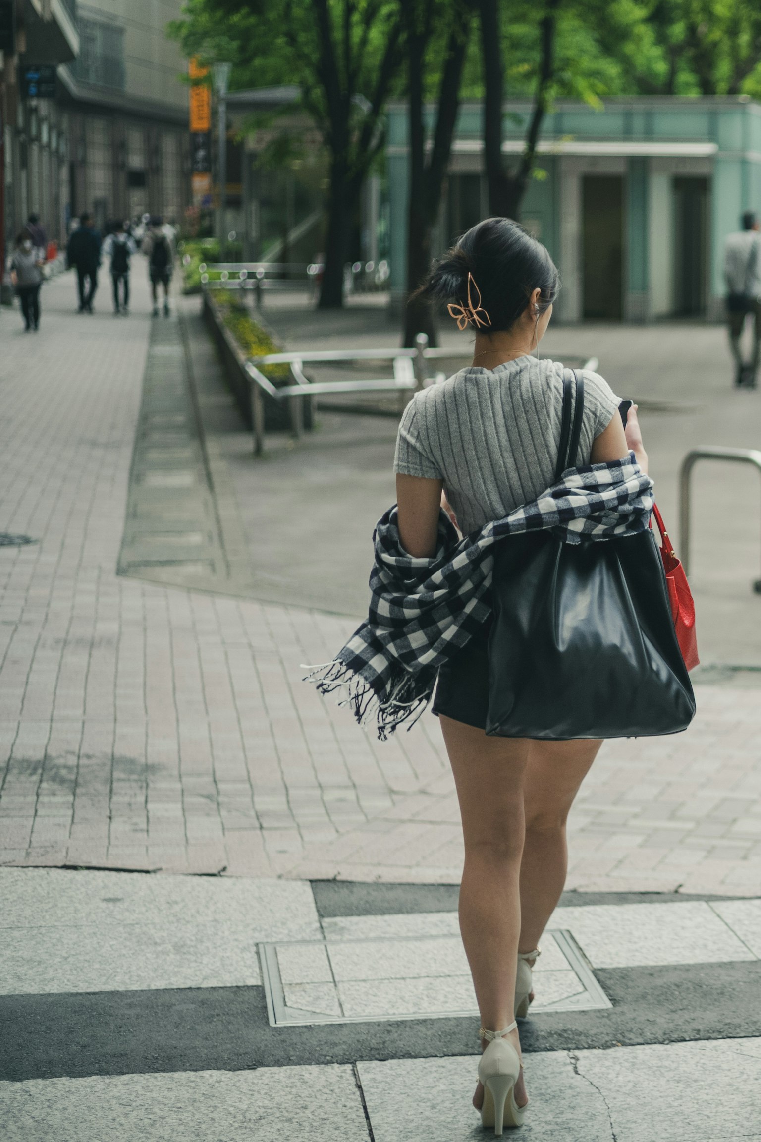 Una donna che cammina nella città con una borsa a spalla e una camicia a quadri