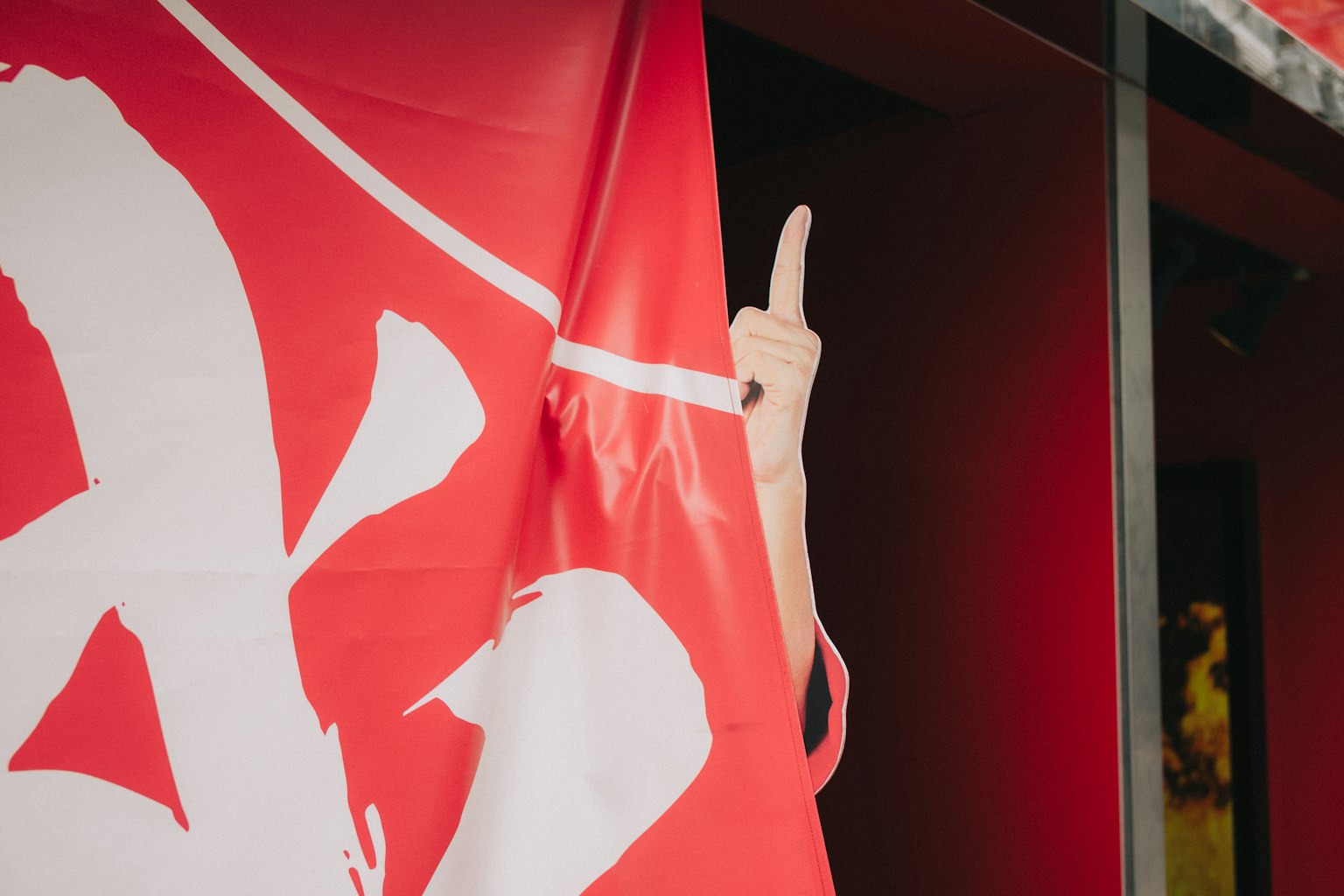 Una mano che mostra il dito medio dietro una bandiera rossa