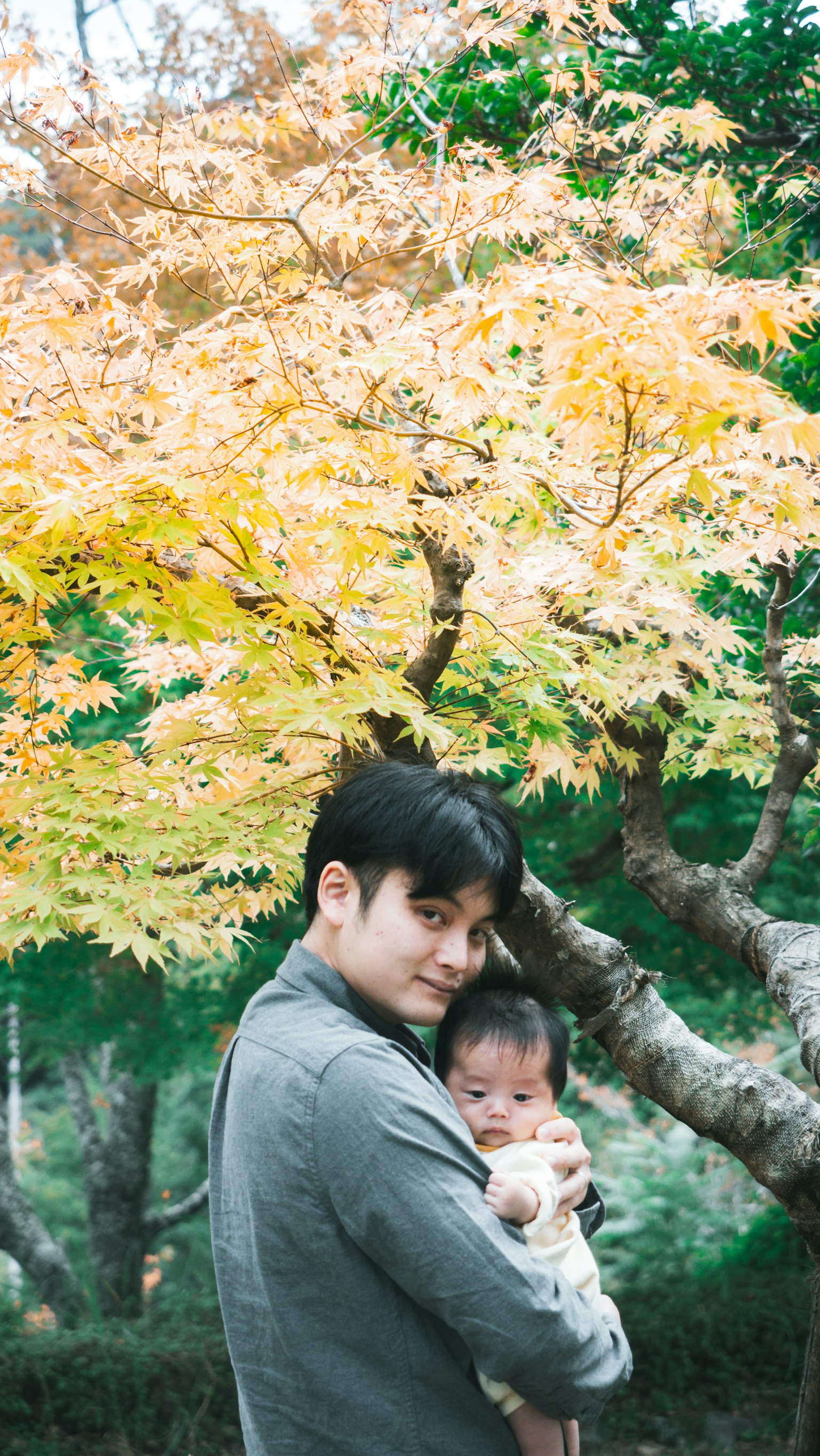 พ่อหนุ่มอุ้มทารกในสวนที่มีใบไม้ฤดูใบไม้ร่วงสวยงาม