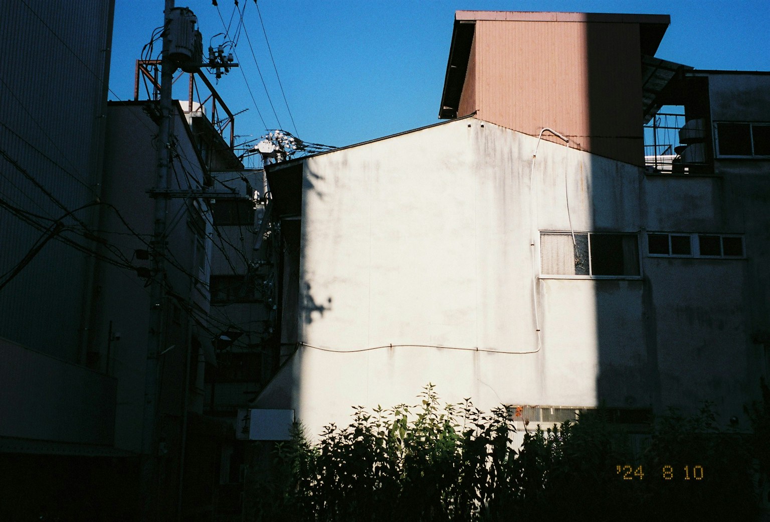 Vue partielle d'un mur d'un vieux bâtiment sous un ciel bleu avec des plantes à l'ombre