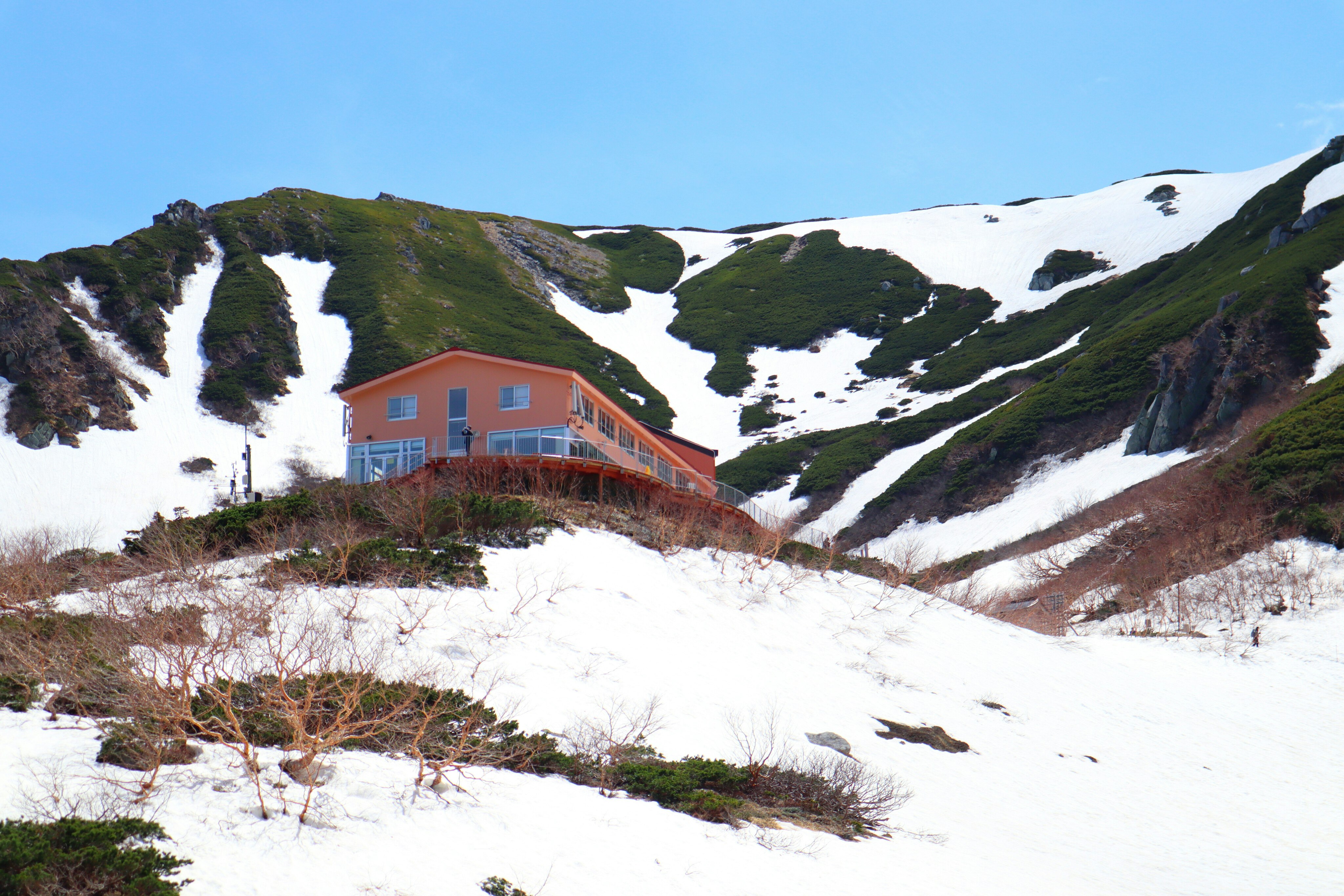 雪に覆われた山の中にある赤い建物と緑の斜面