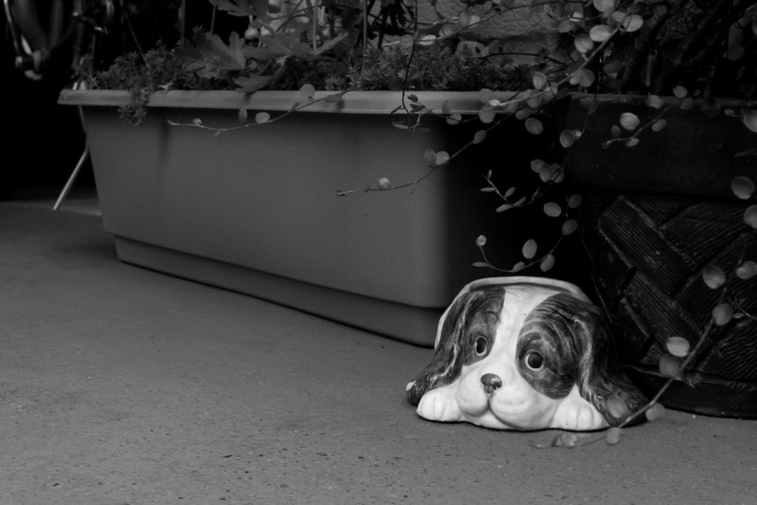 Eine schwarz-weiße Hundefigur, die neben einem Blumentopf liegt