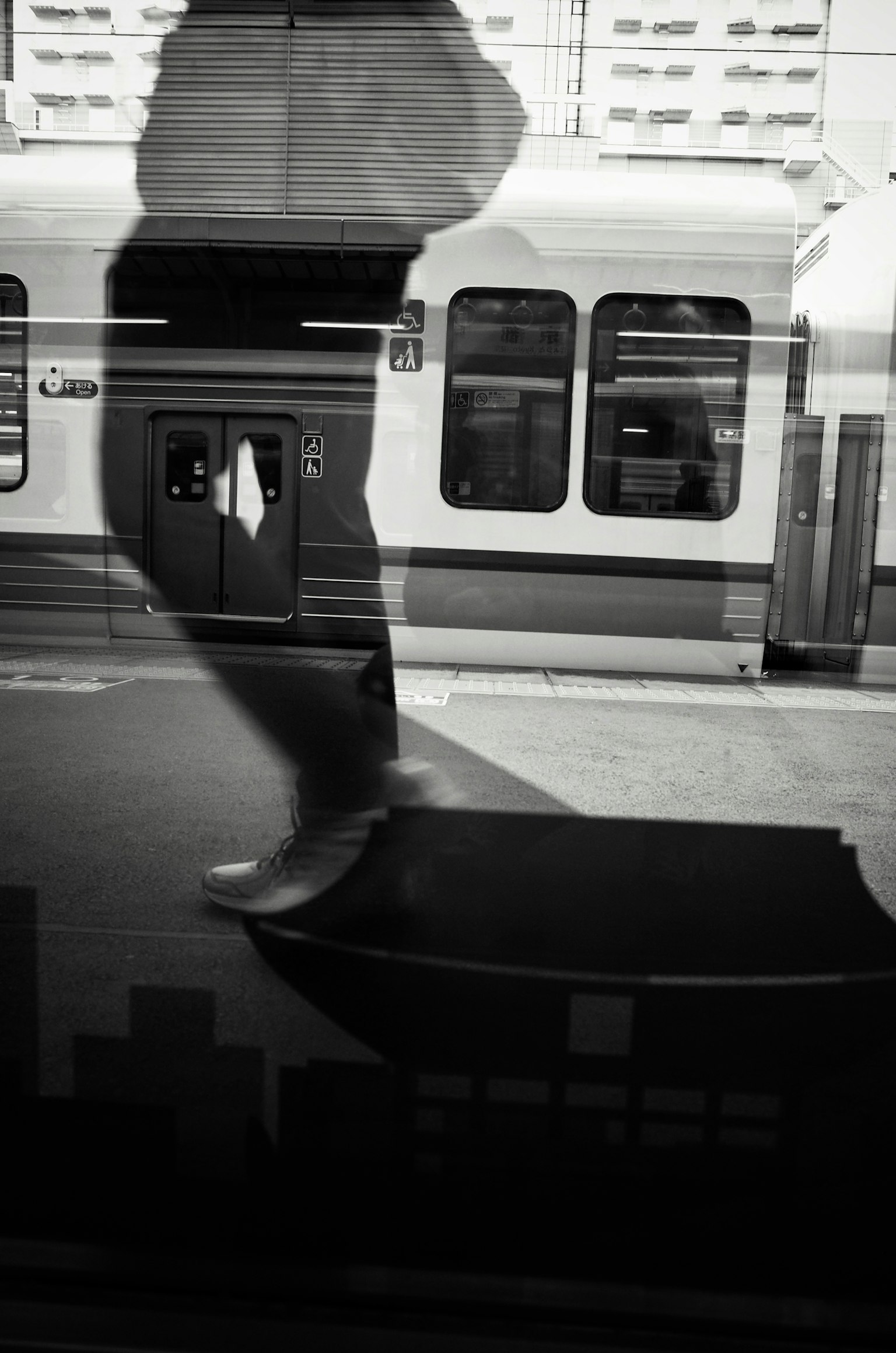 A shadow of a person walking reflected in a train window in black and white