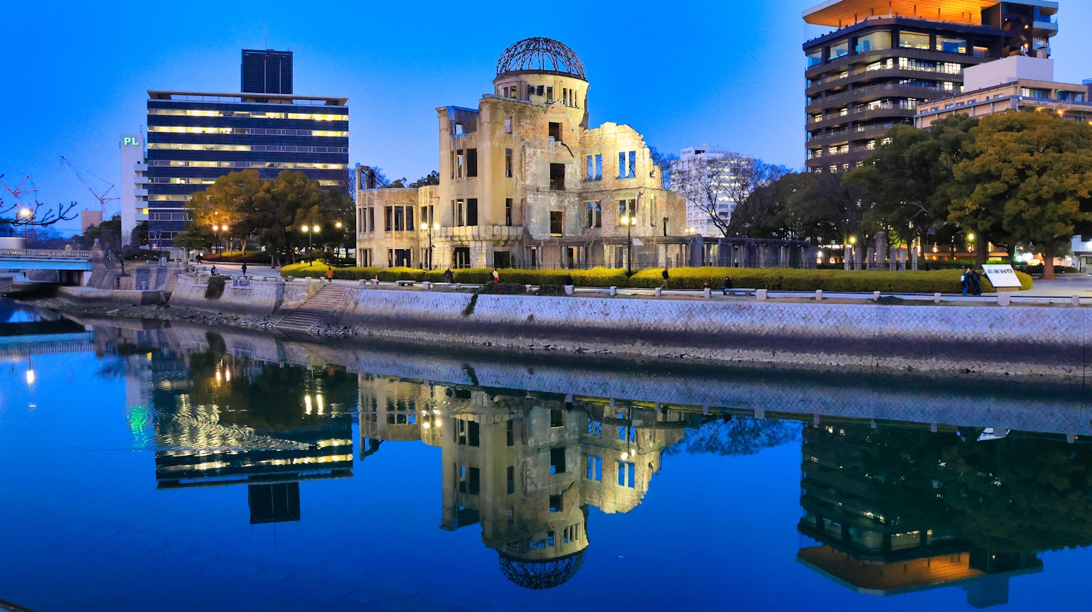 Edificio storico lungo il fiume con grattacieli moderni che si riflettono nell'acqua sotto un cielo blu