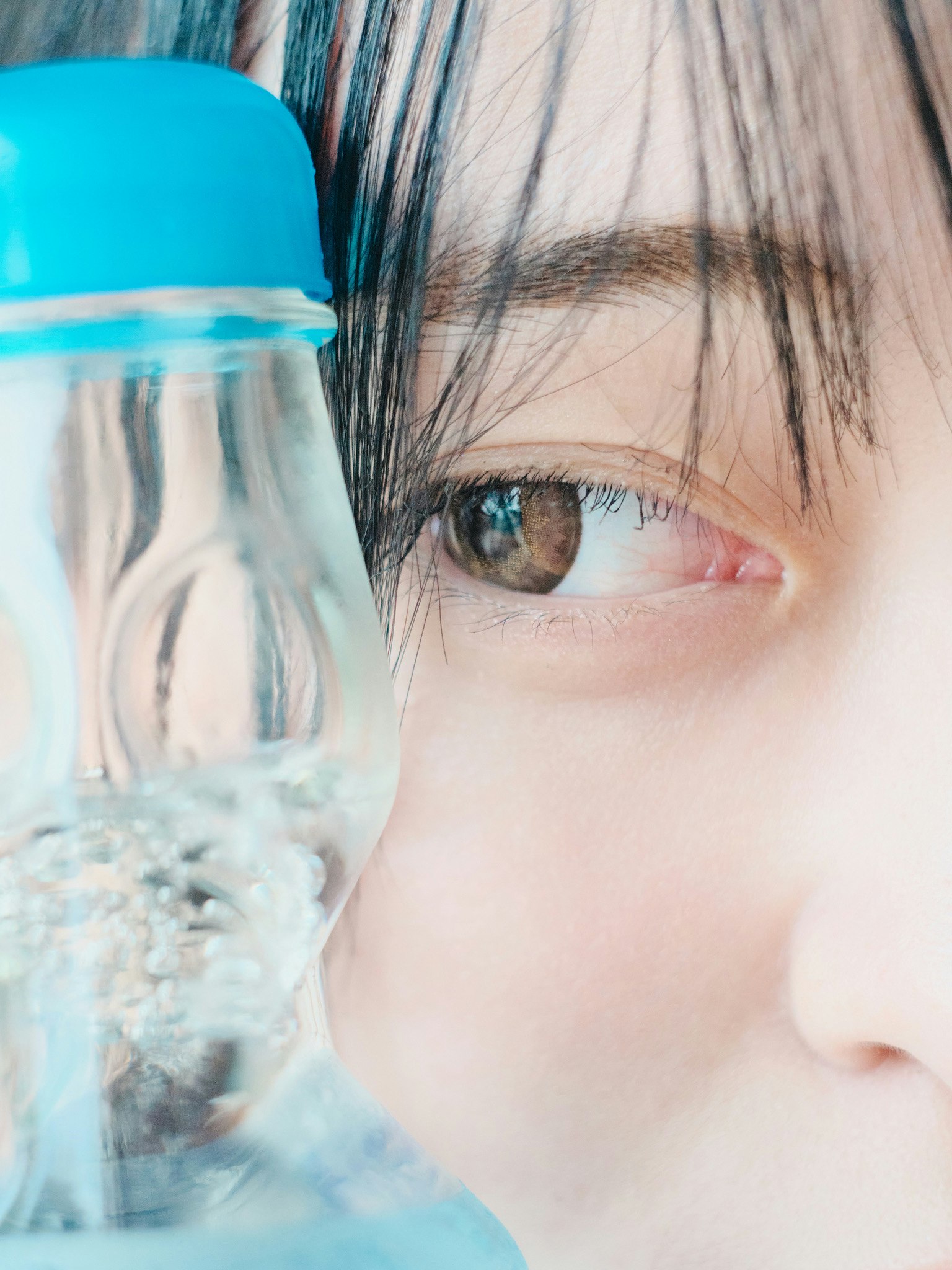水のボトルを持つ女性の顔のクローズアップ 目の色は茶色で髪は黒