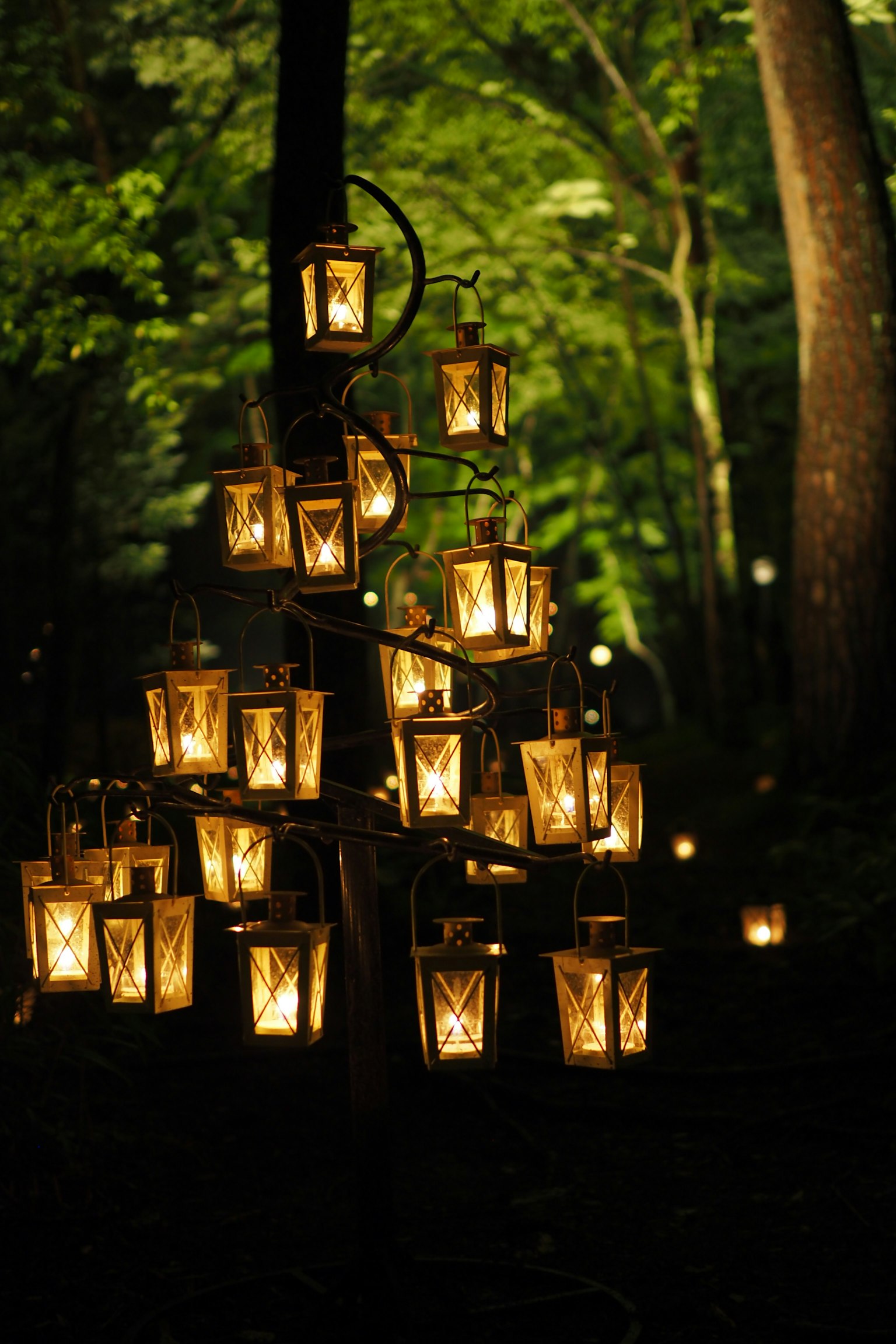 Decorative lamp stand with multiple glowing lanterns in a green forest
