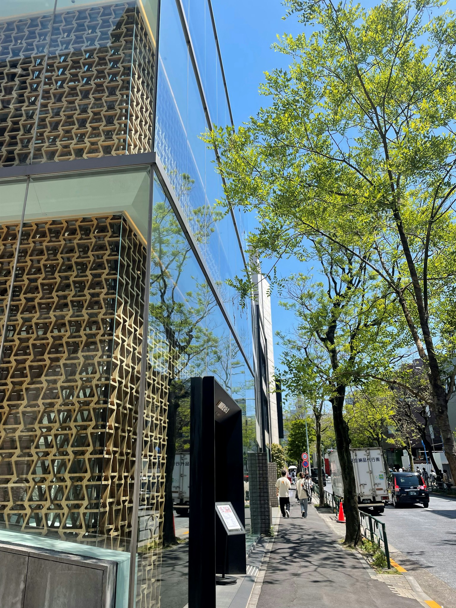 展示現代建築外觀的圖像，面向街道，具有編織設計的牆壁和藍天下的綠色樹木