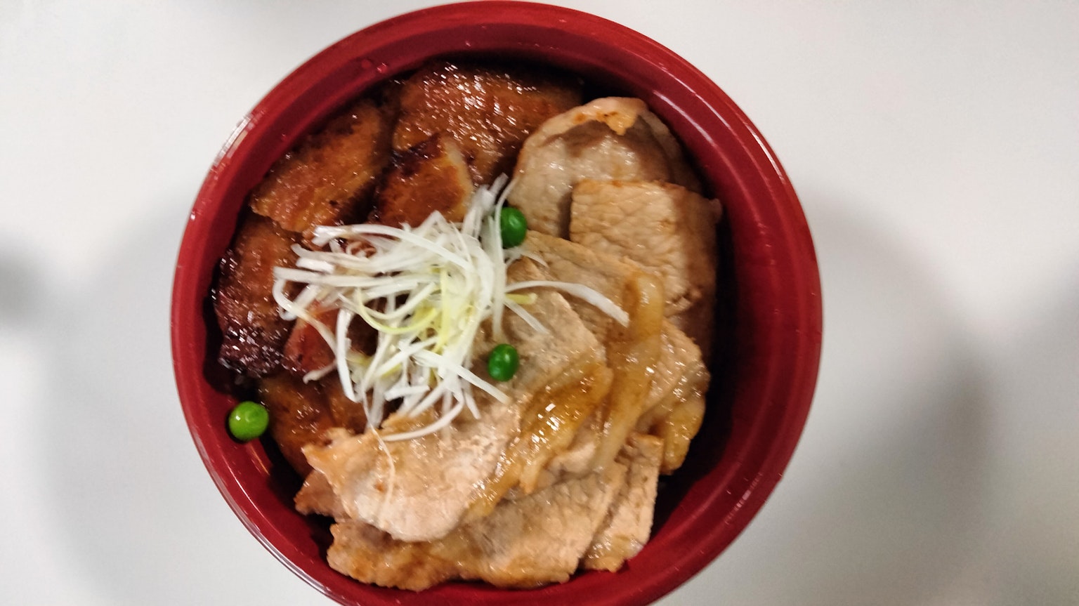 Ciotola di maiale e pollo servita in un piatto rosso Pollo fritto con cipollotti e piselli come guarnizioni