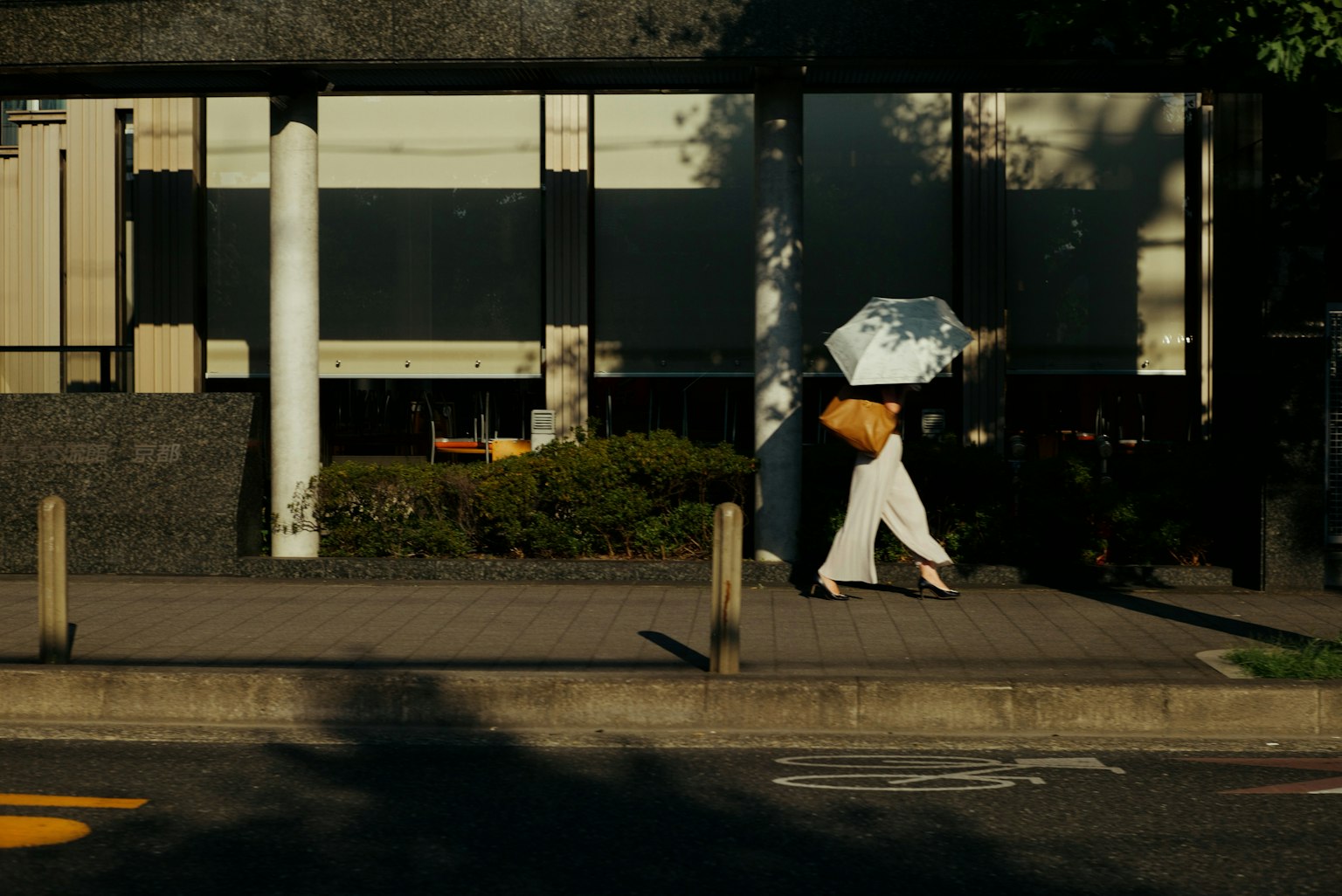 A woman in white clothing walking with an umbrella in an urban setting