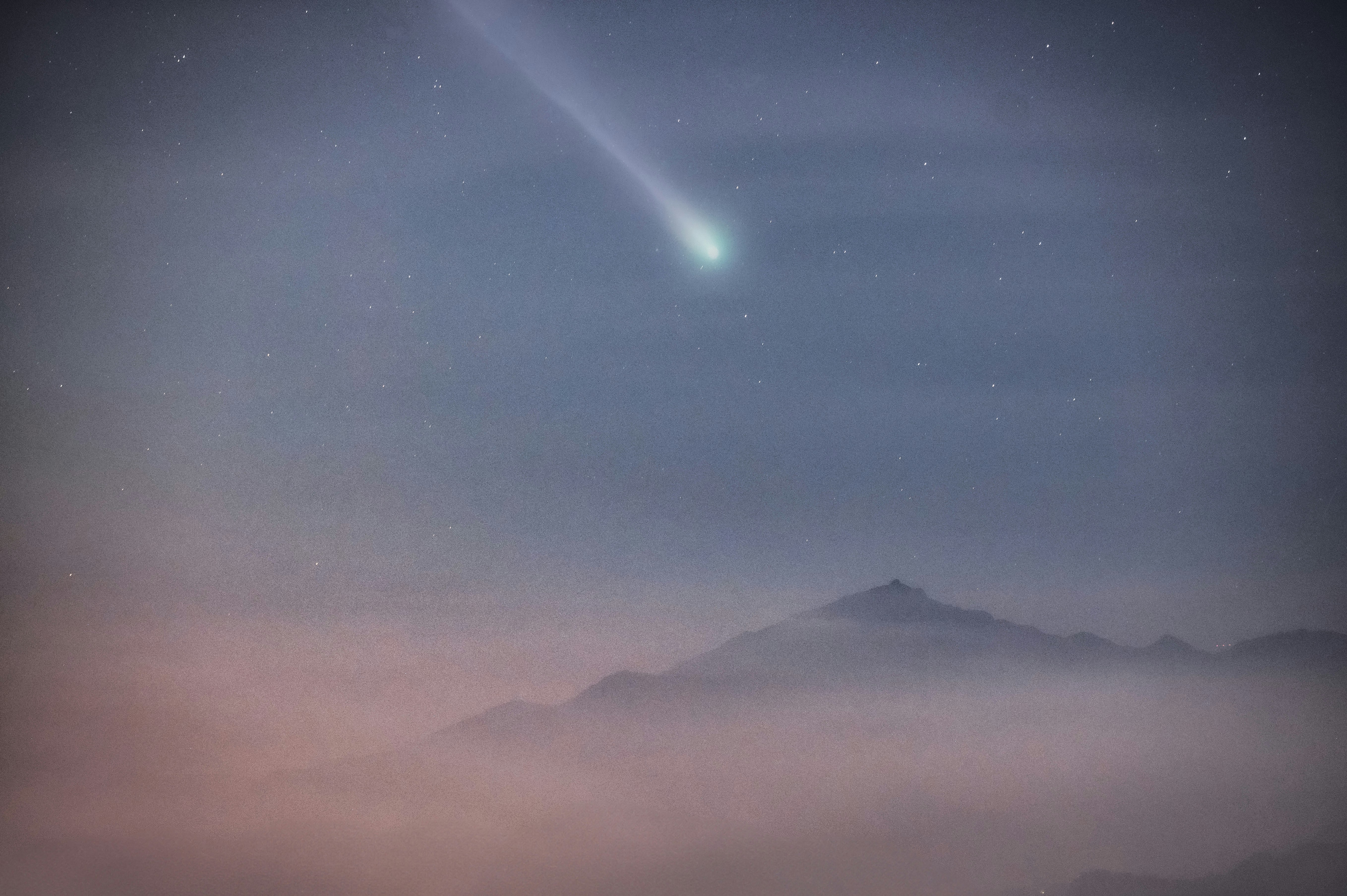 霧のかかった山並みと流星が見える夜空