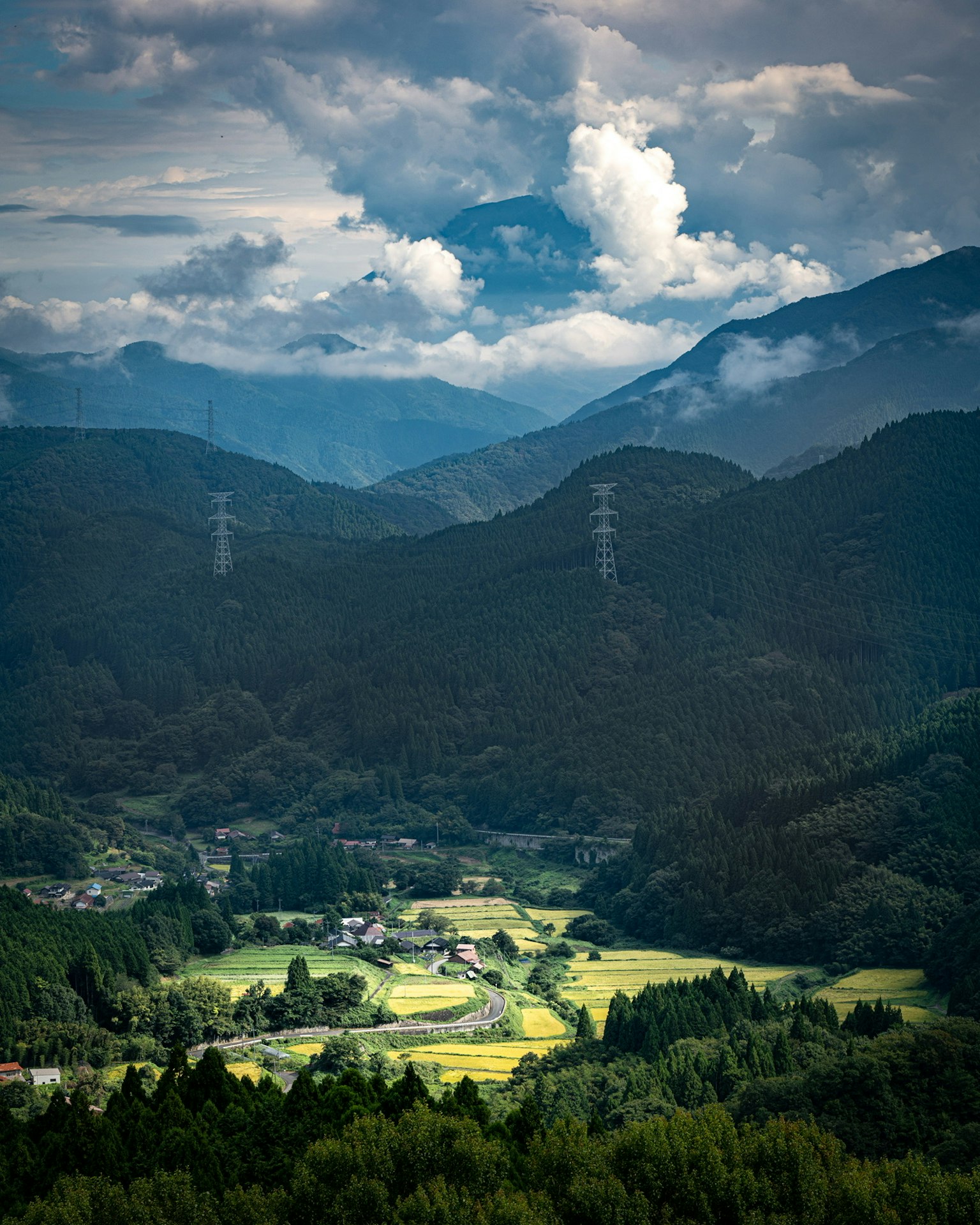 群山和雲彩環繞著一片郁郁蔥蔥的山谷的美景