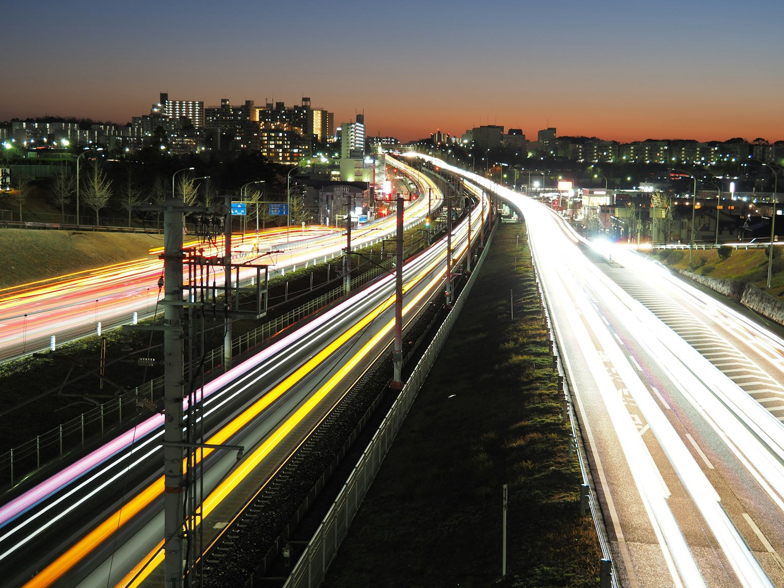 夜景の高速道路と鉄道の動きが鮮やかに映る都市の風景