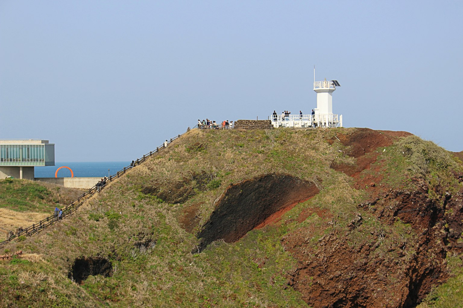 Coastal landscape featuring a lighthouse and people gathering on a hill
