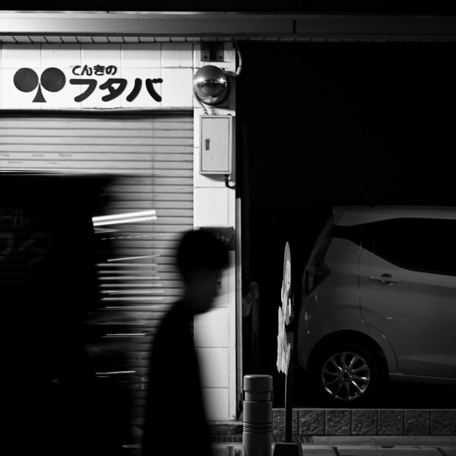 ป้ายร้านในเวลากลางคืนพร้อมเงาของคนที่เดิน