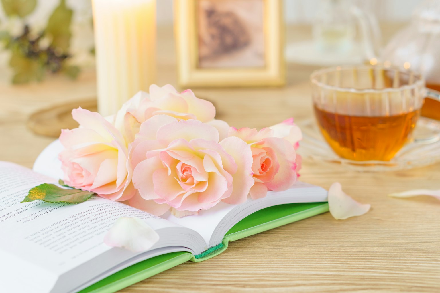 A scene with pink roses on an open book a lit candle and a cup of tea