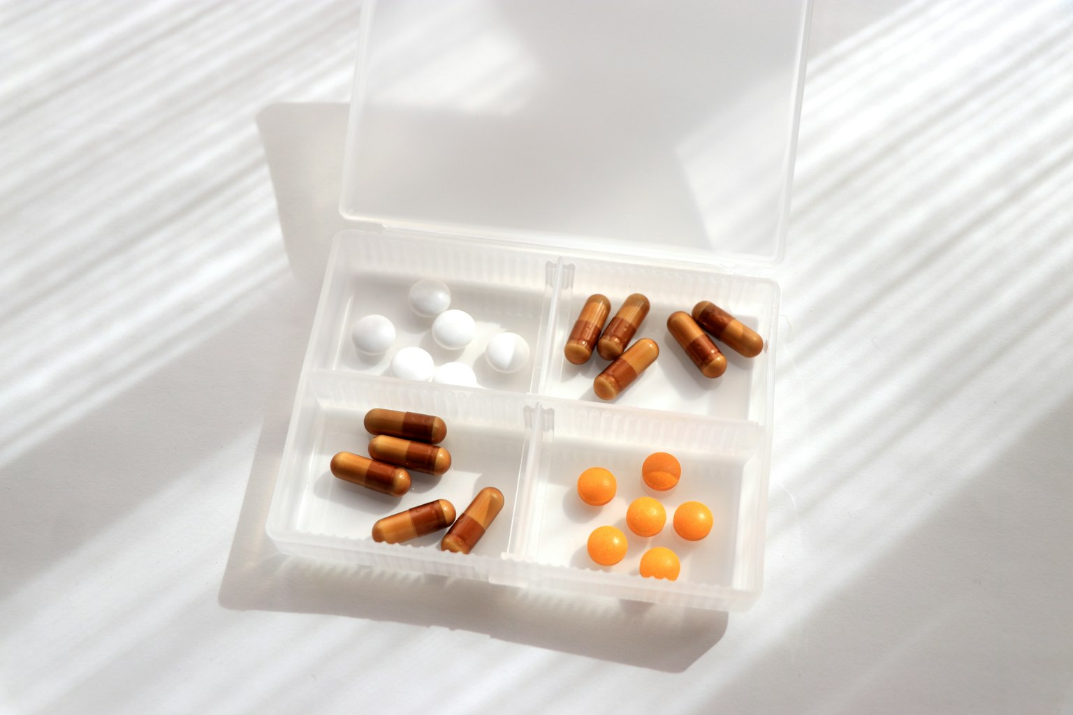 Un organizer per pillole bianco con capsule marroni e compresse arancioni disposte all'interno