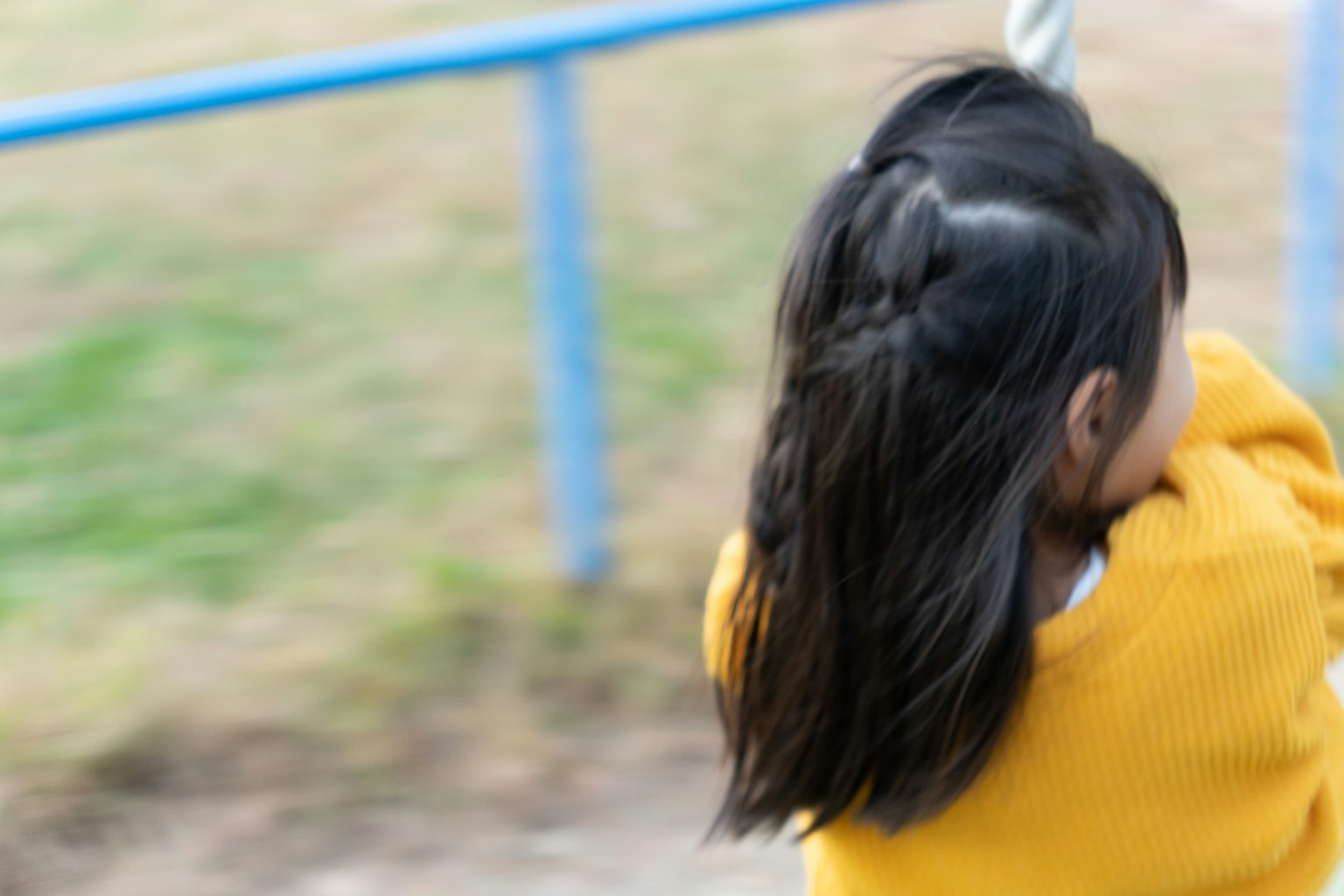 Child in a yellow sweater riding a swing from behind
