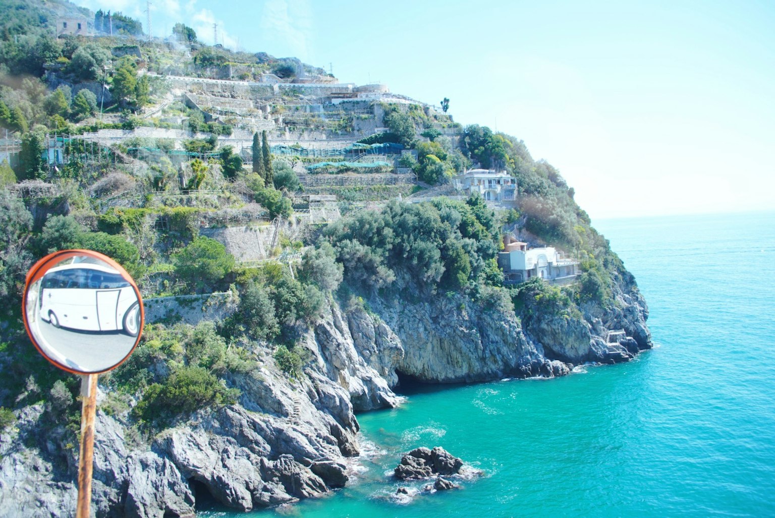 Scenic view of a lush cliff along the coastline with blue sea and a reflective mirror in the foreground