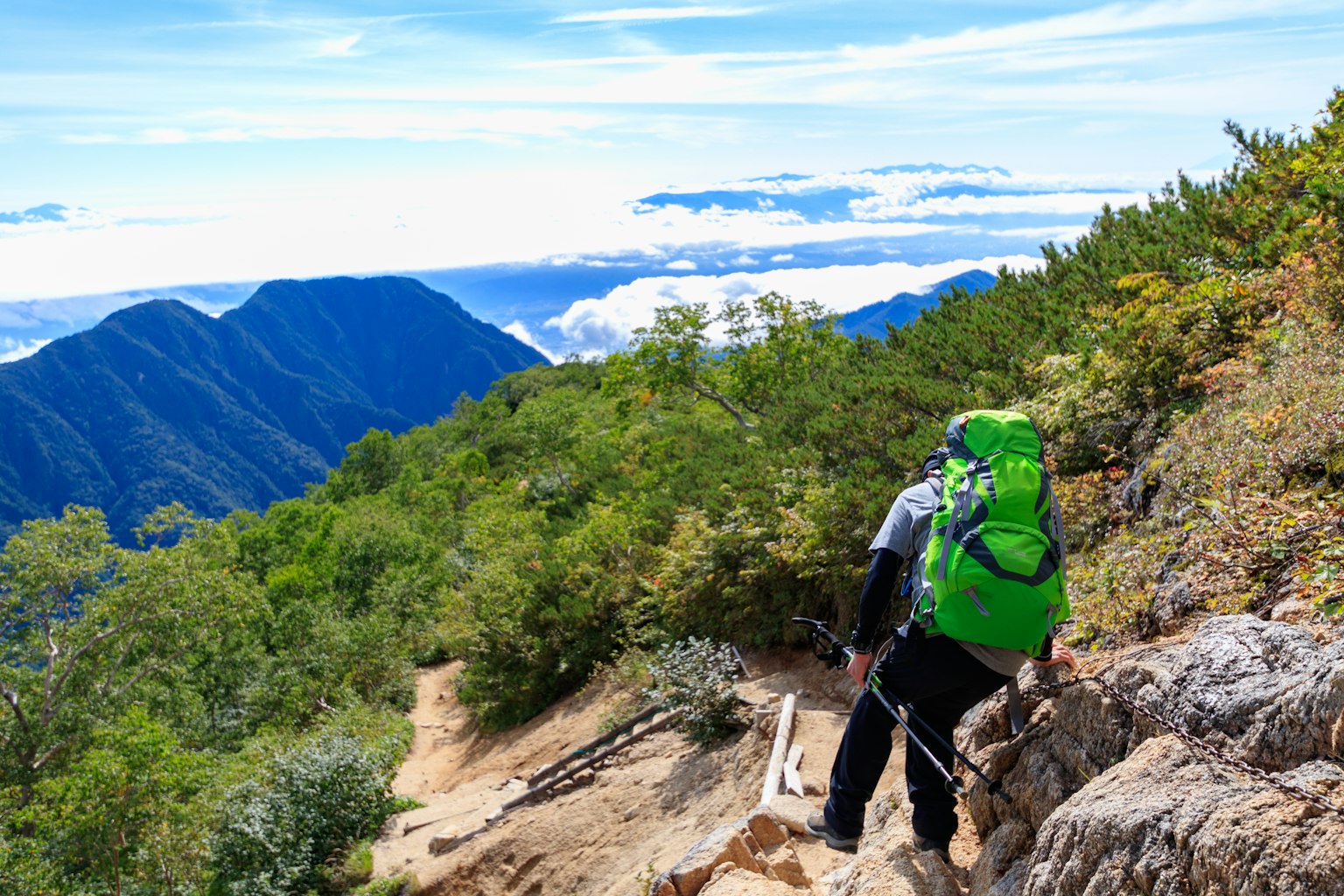Pendaki dengan ransel hijau sedang mendaki jalur gunung