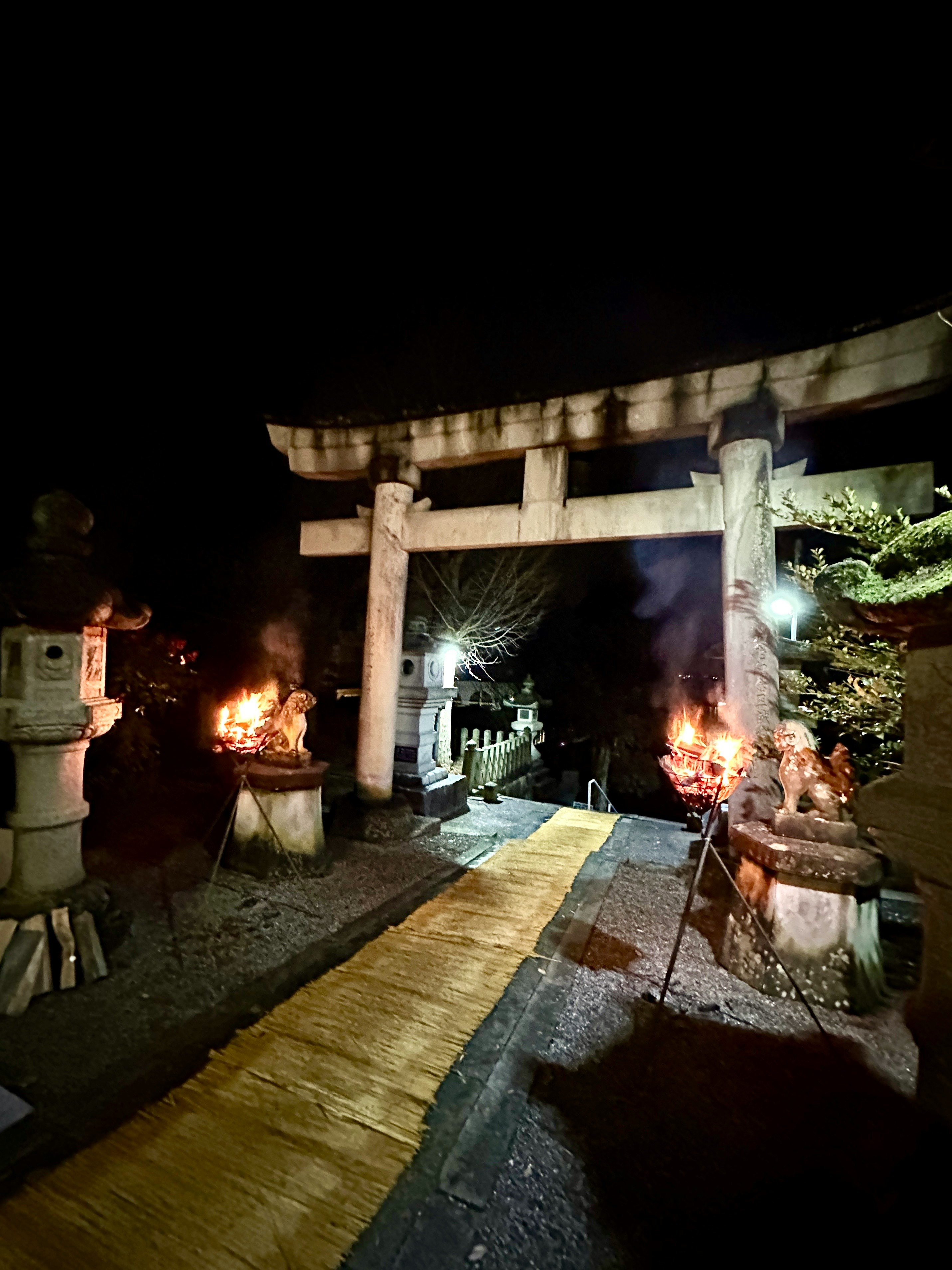 鳥居のある神社の参道で焚き火と提灯が灯る初詣の夜