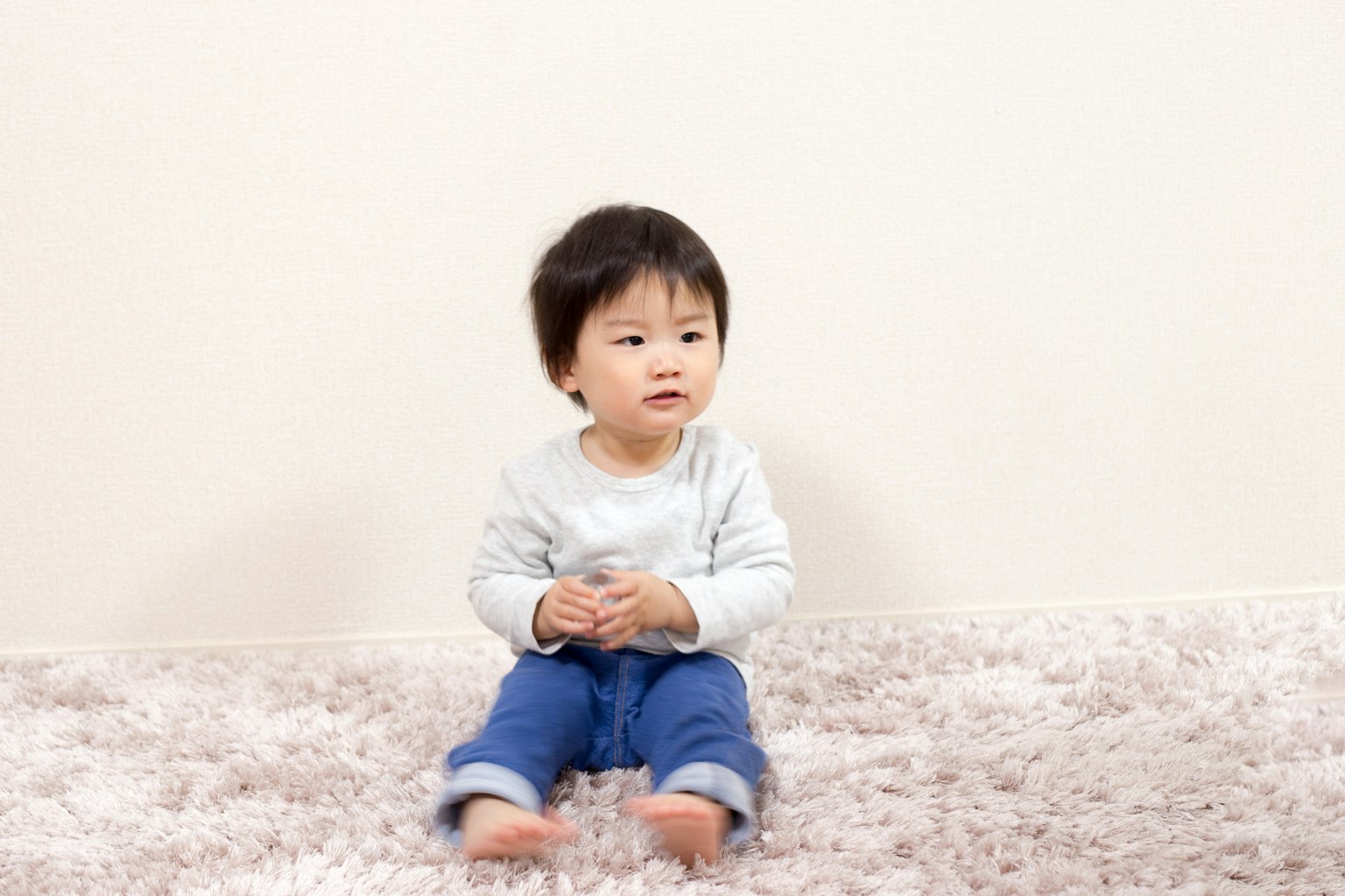 A young child sitting on a soft rug in front of a plain wall