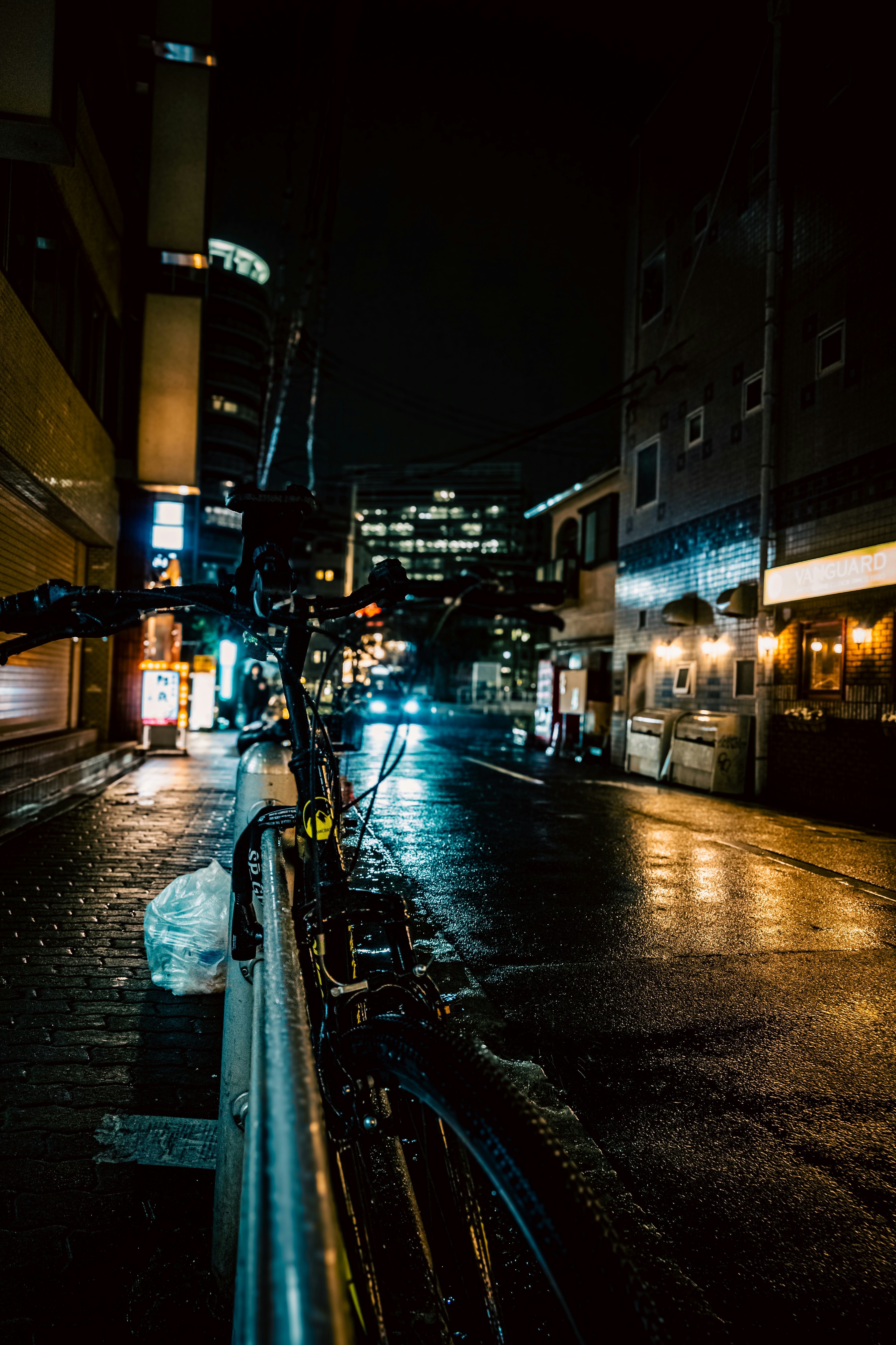 雨の夜の路地に並ぶ自転車とネオンの街並み