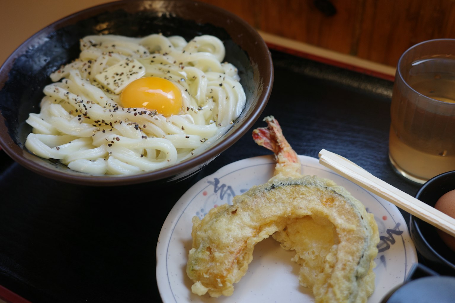 Un bol de nouilles udon avec un œuf cru et une assiette de tempura de crevettes et de légumes