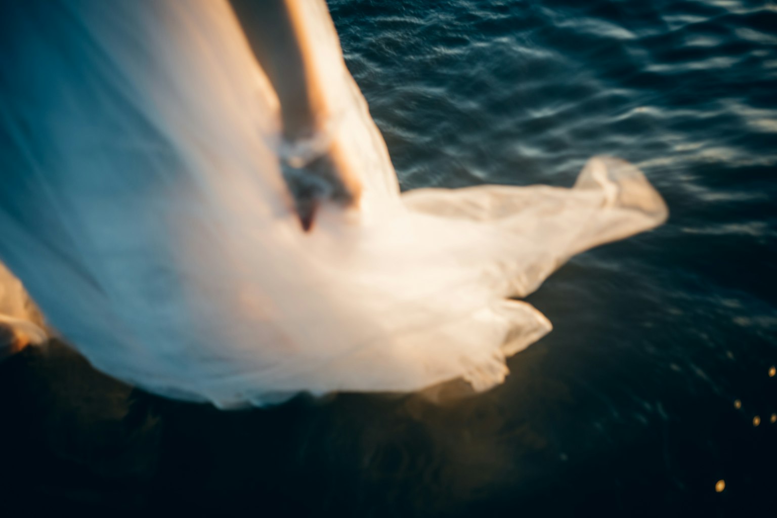 A hand holding a flowing white dress near the water