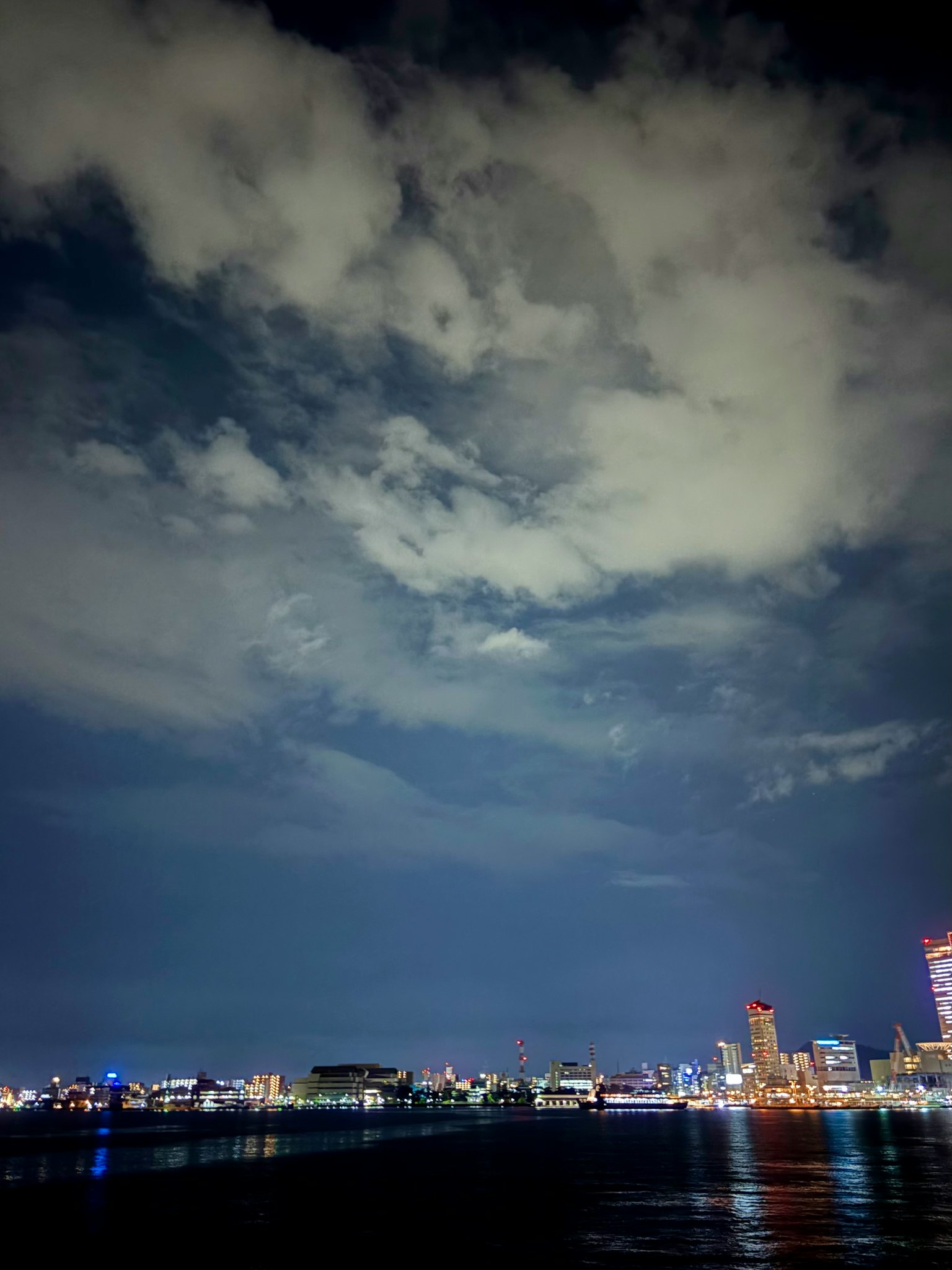 夜の海と都市の明かりが映る風景 雲が広がる空