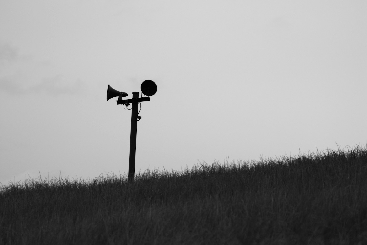 Silueta de una sirena de advertencia y un altavoz contra un paisaje en blanco y negro
