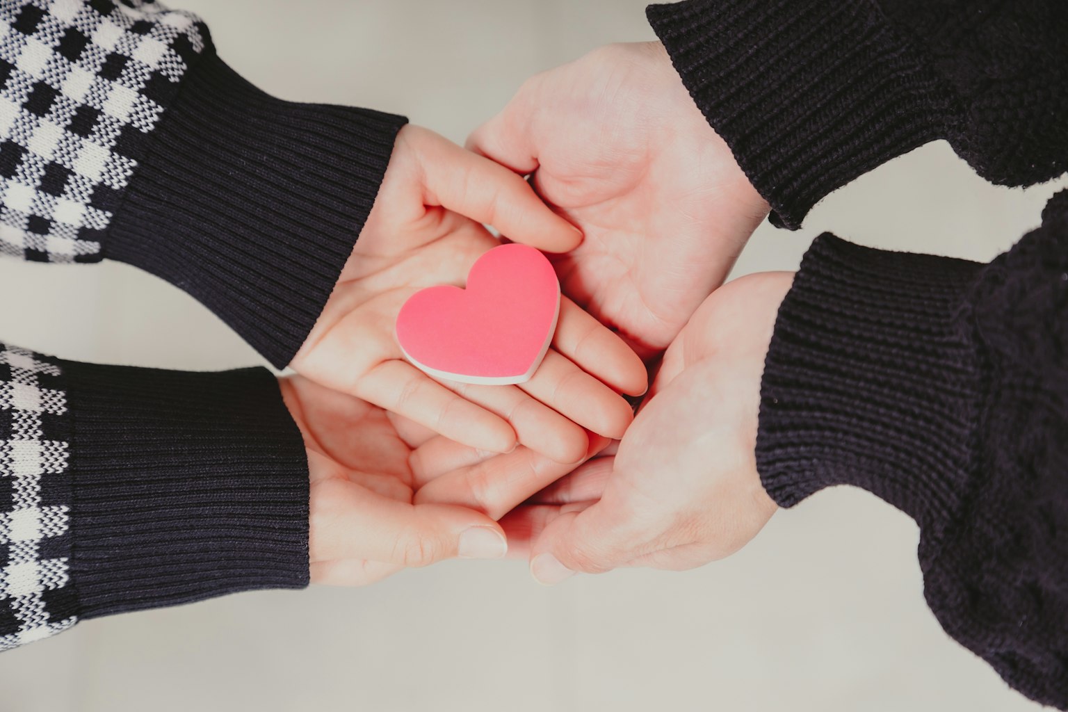 Due mani che tengono una forma di cuore rosa tra di loro