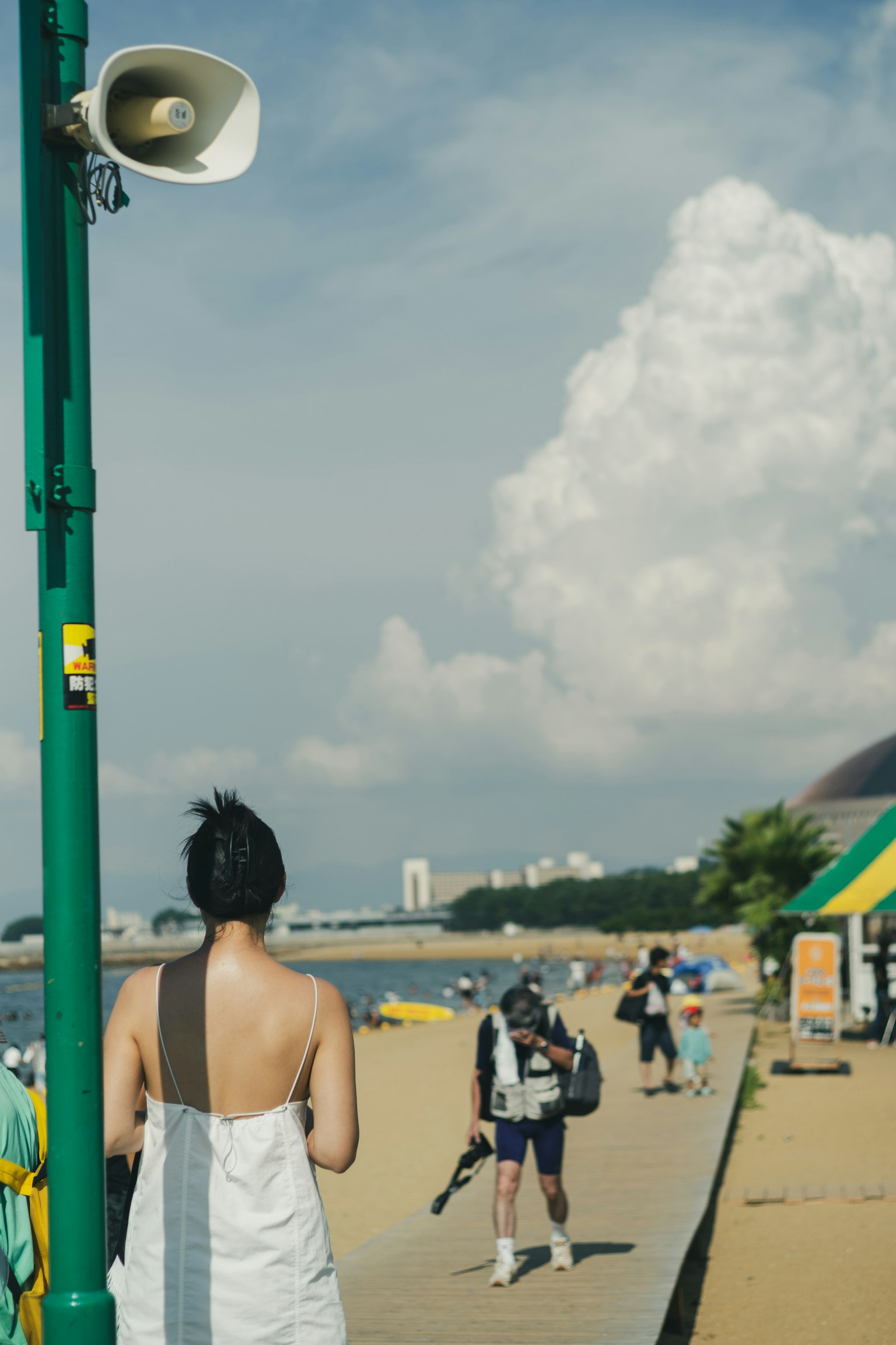 A woman standing with her back to the camera on a beach with a cloudy sky