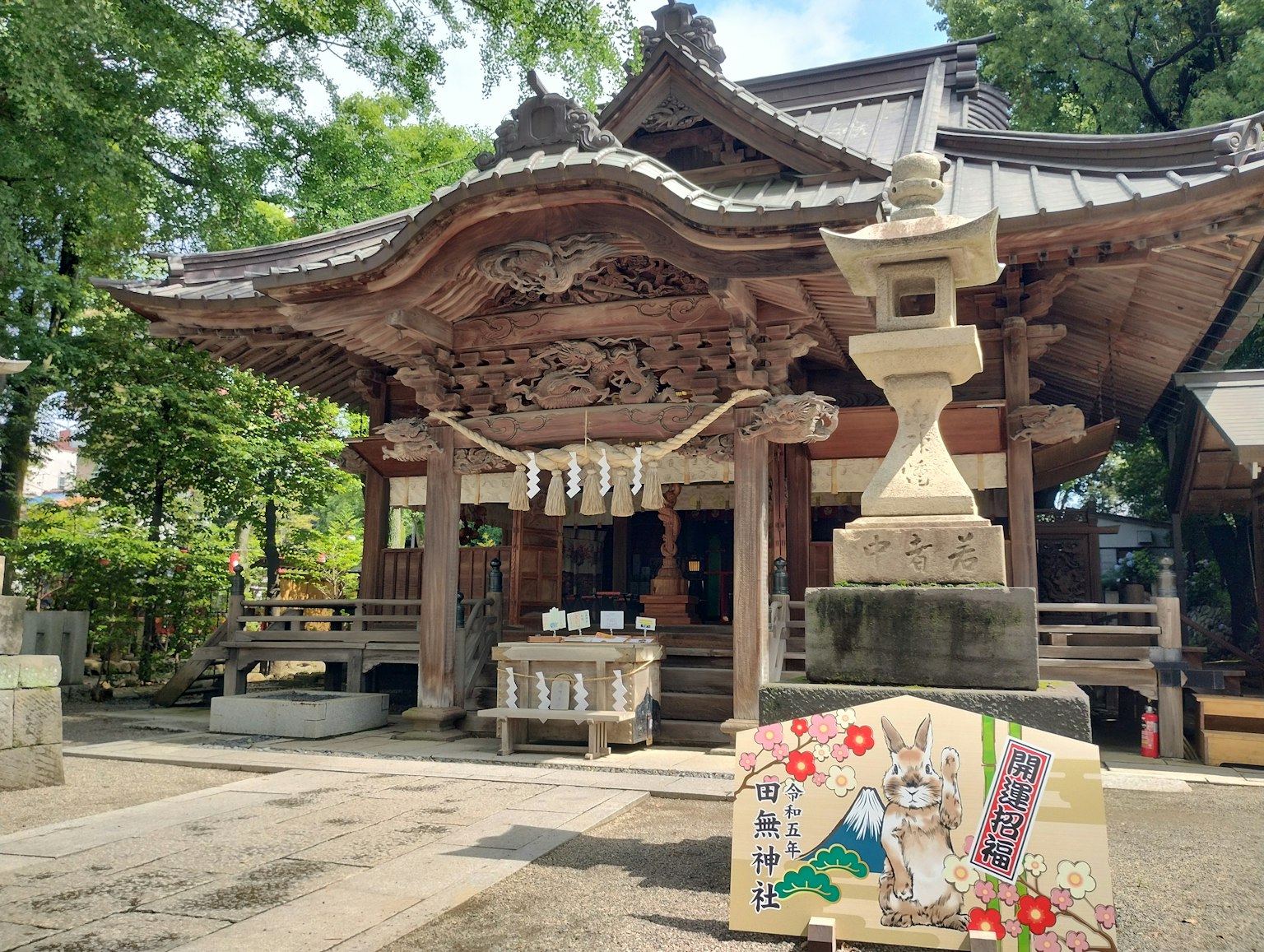 美丽的神社外观，周围环绕着郁郁葱葱的绿树，配有石灯笼和装饰性招牌