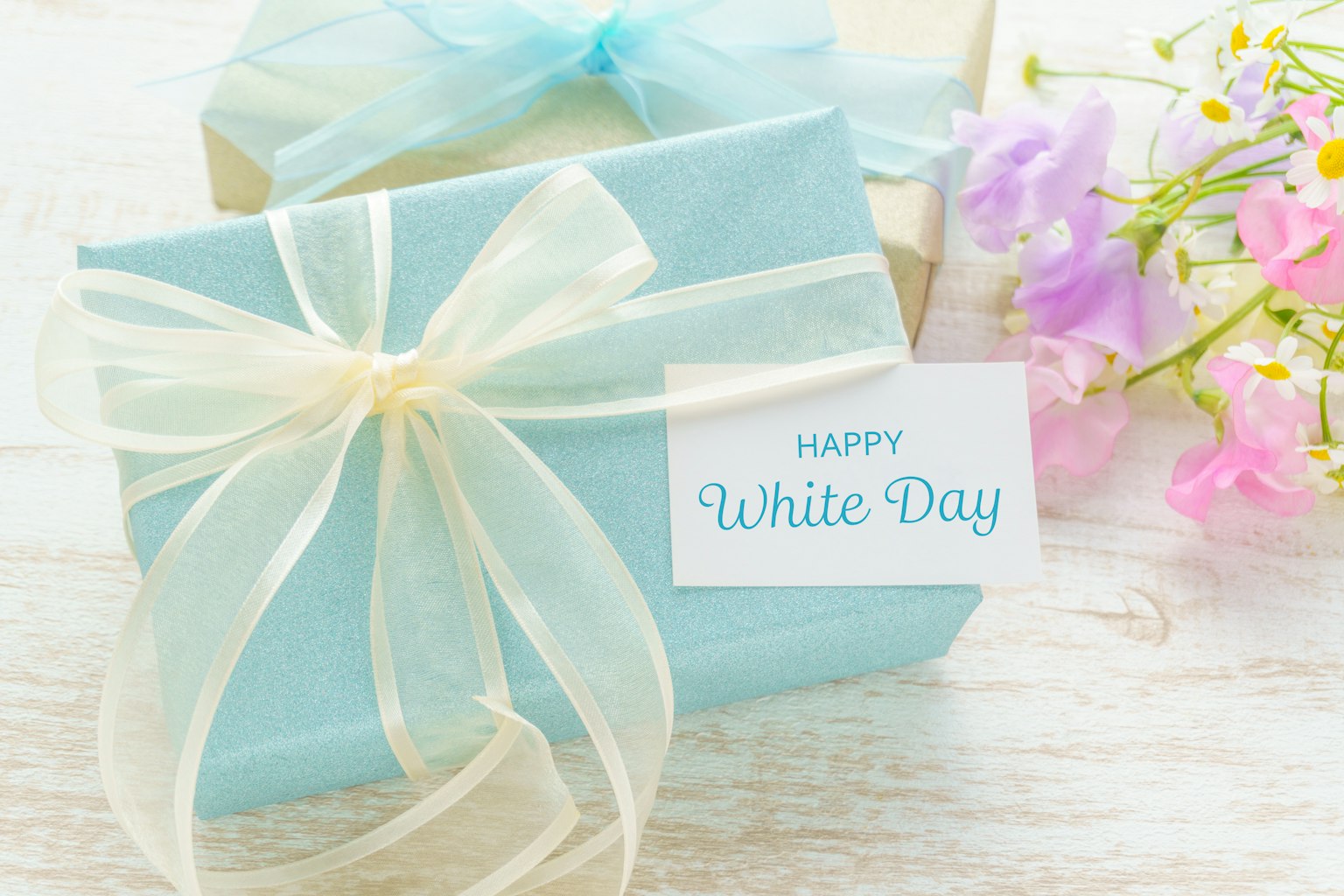 Blue wrapped gift boxes with a card saying Happy White Day and flowers