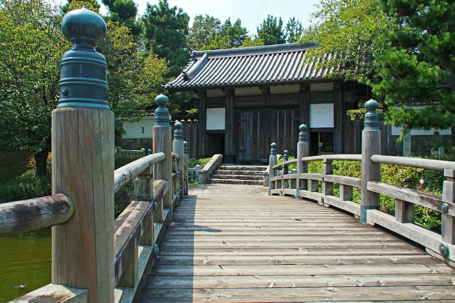 Wooden bridge leading to a traditional building surrounded by greenery