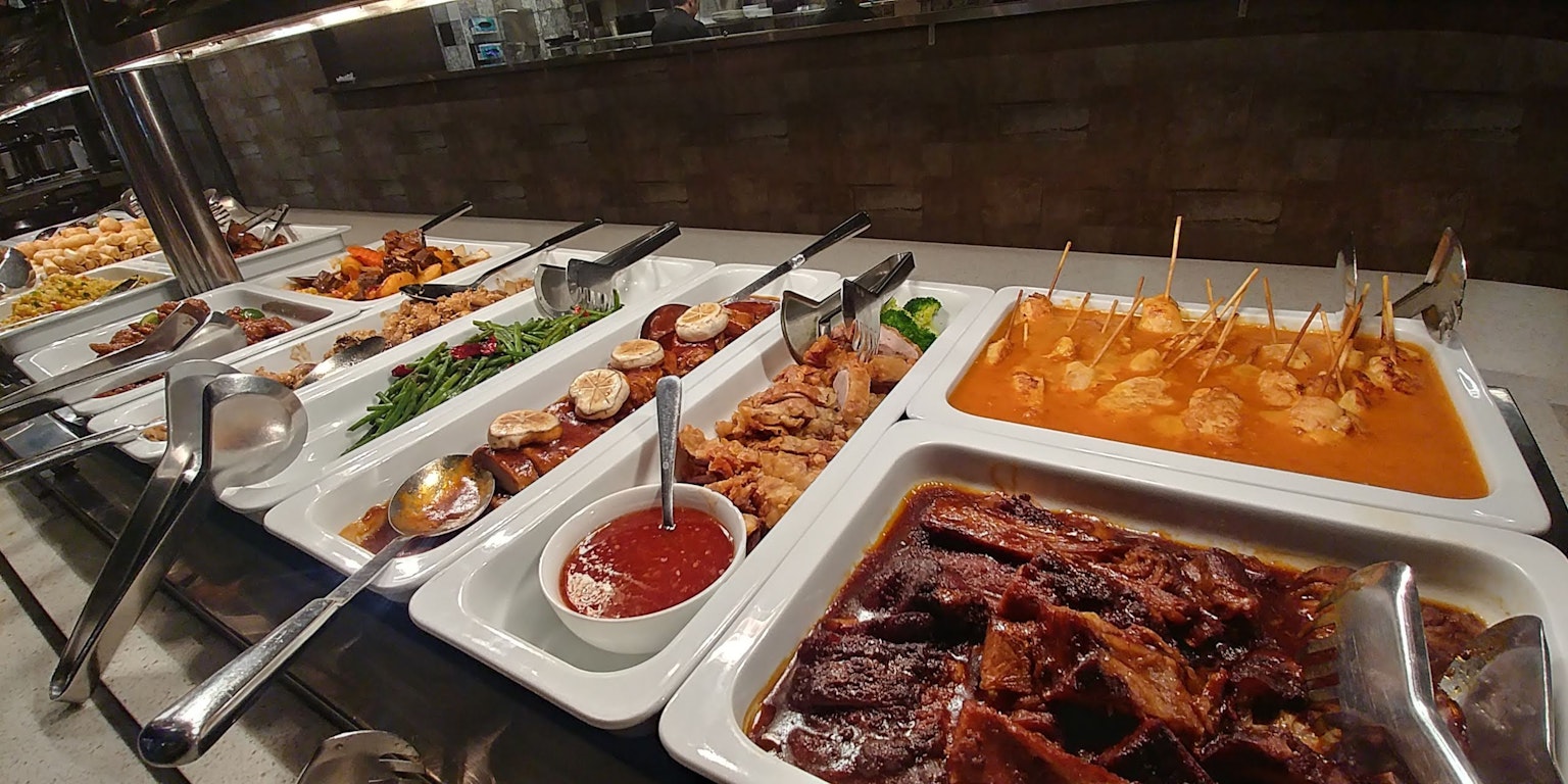 Larga mesa de buffet llena de varios platos incluyendo carnes y salsas