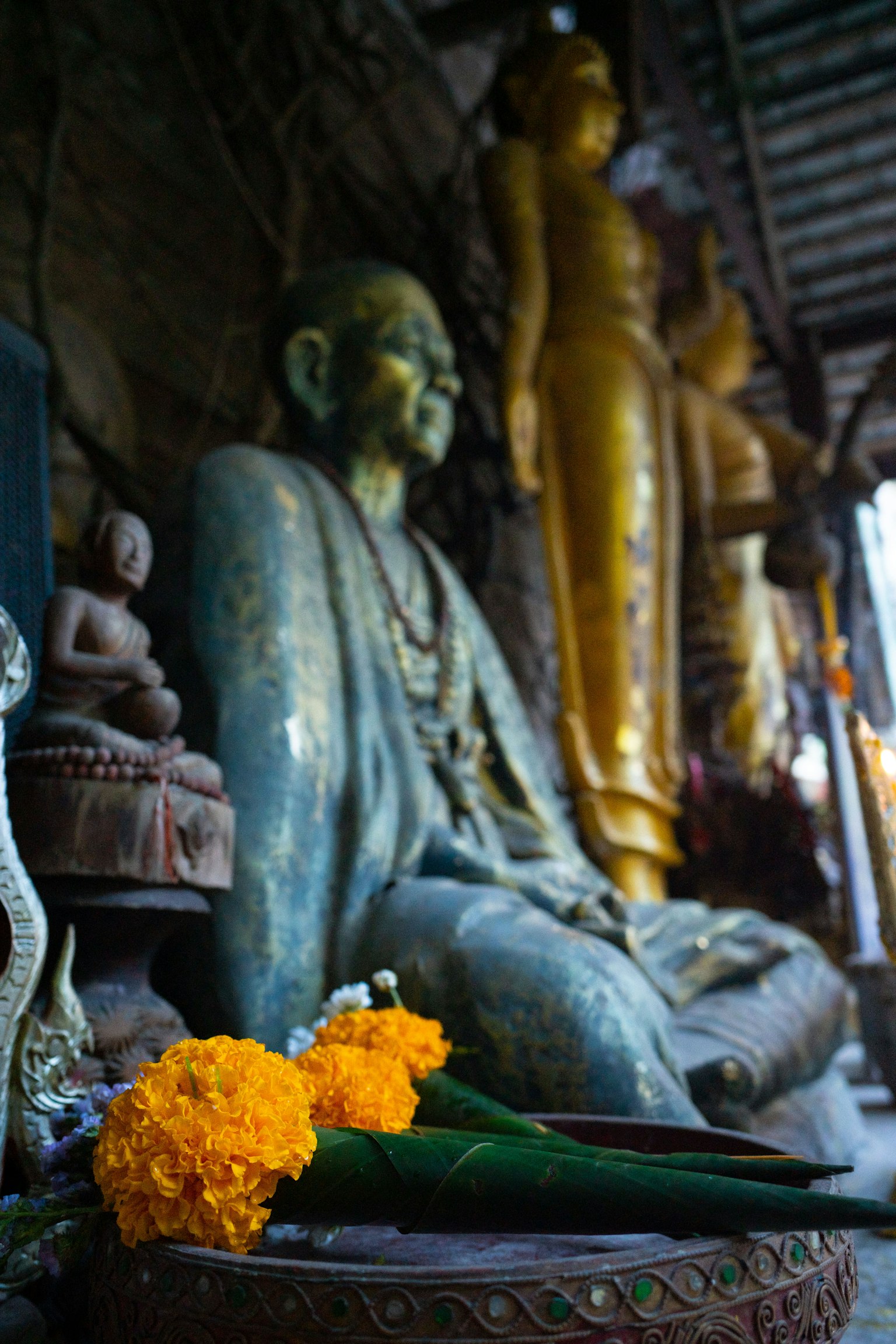 Patung Buddha perunggu dengan persembahan bunga kuning di dalam kuil dengan patung emas