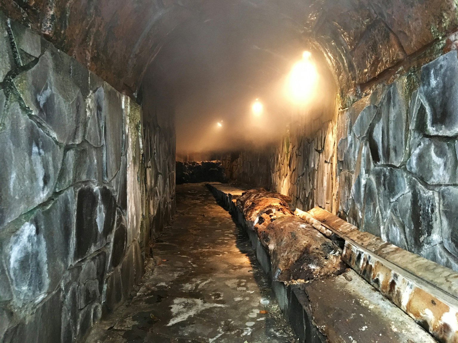Interno di un tunnel umido con muri di pietra e passaggio illuminato
