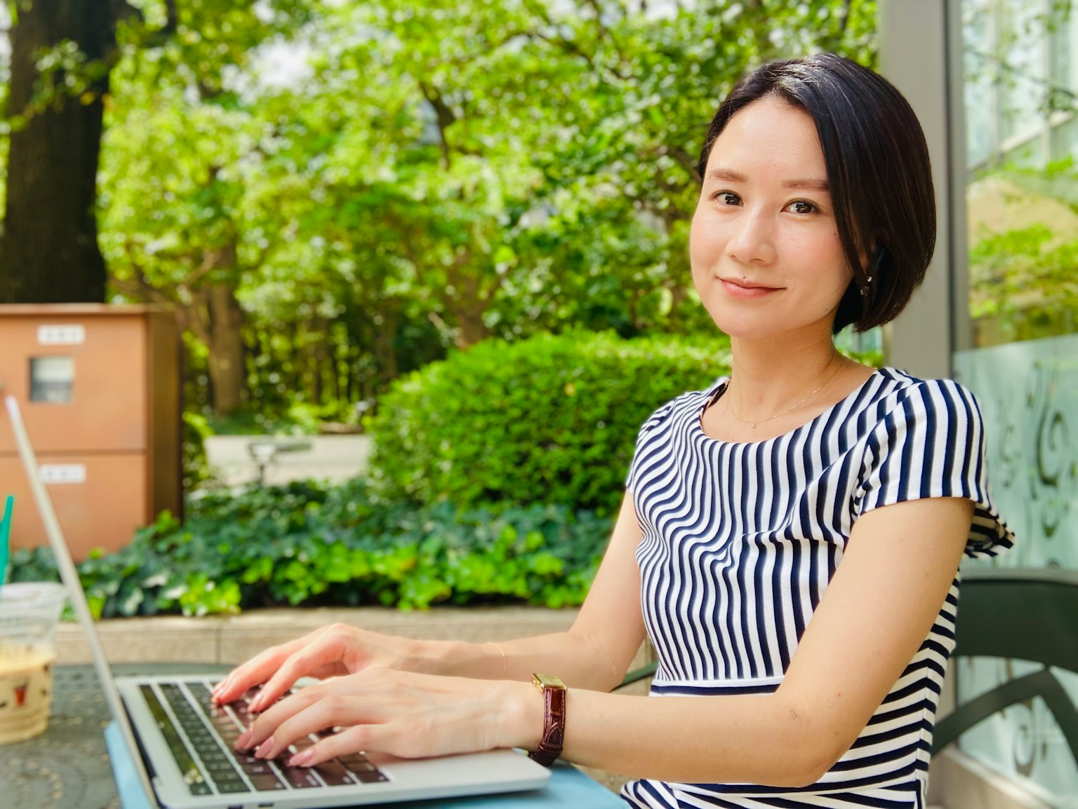 在公園裡使用筆記型電腦的女性 綠色背景 條紋襯衫