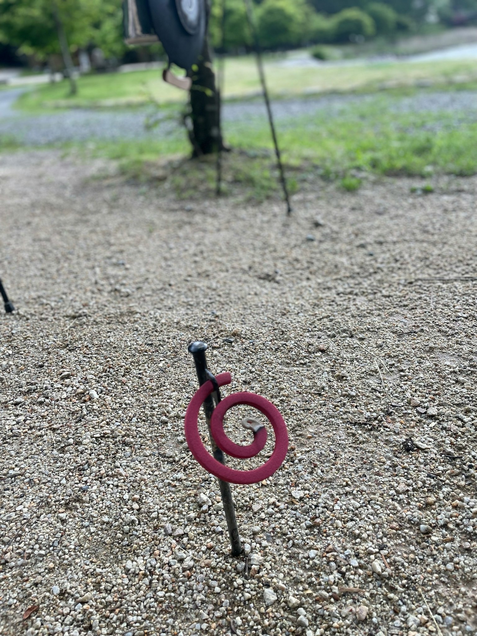 Un objeto metálico rojo en espiral en el suelo con un paisaje verde de fondo
