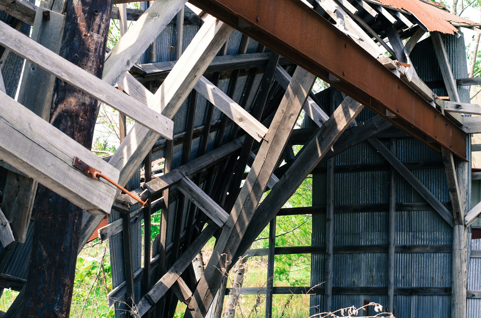 Detalles interiores de una estructura de madera en ruinas con componentes metálicos oxidados y un fondo verde