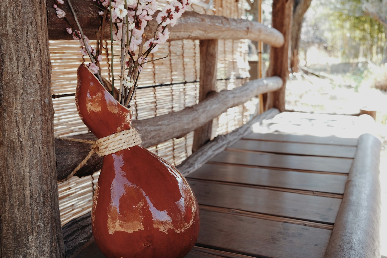 Jarrón de cerámica roja con flores sobre una mesa de madera en un entorno rústico